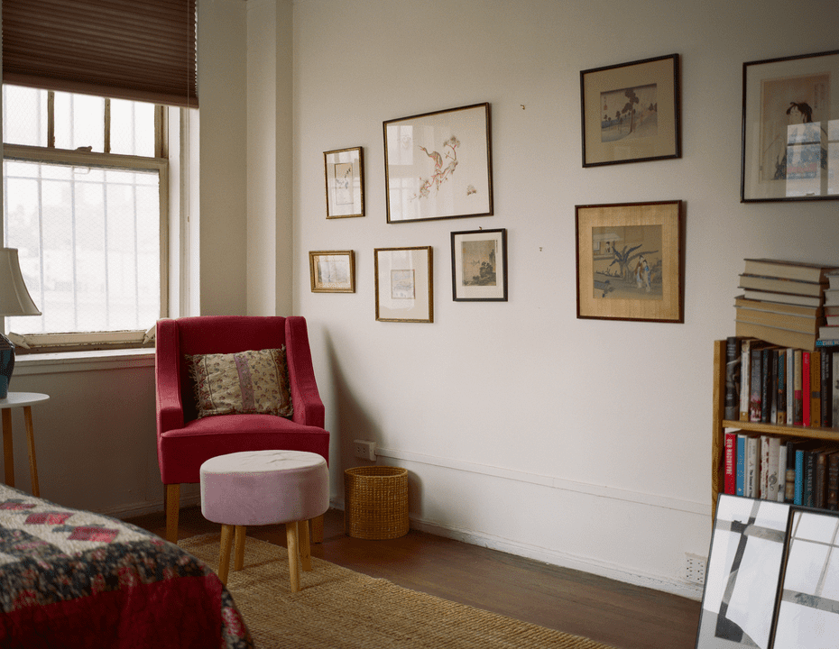 Blick in ein Schlafzimmer mit rotem Samtstuhl und Zeichnungen an der Wand