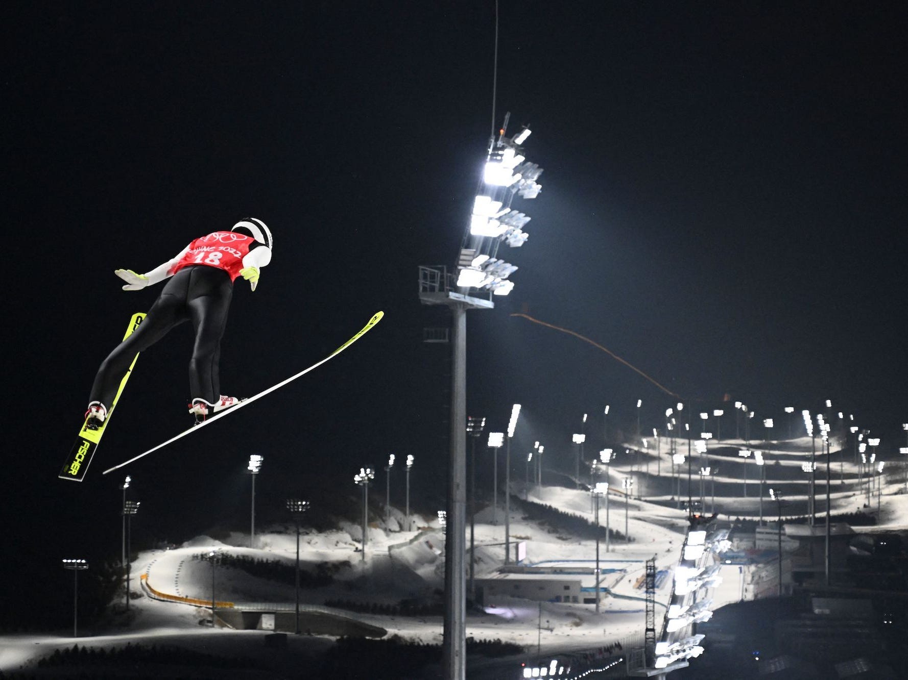 Ein Skispringer springt in die Luft und blickt auf die Olympiastrecke.