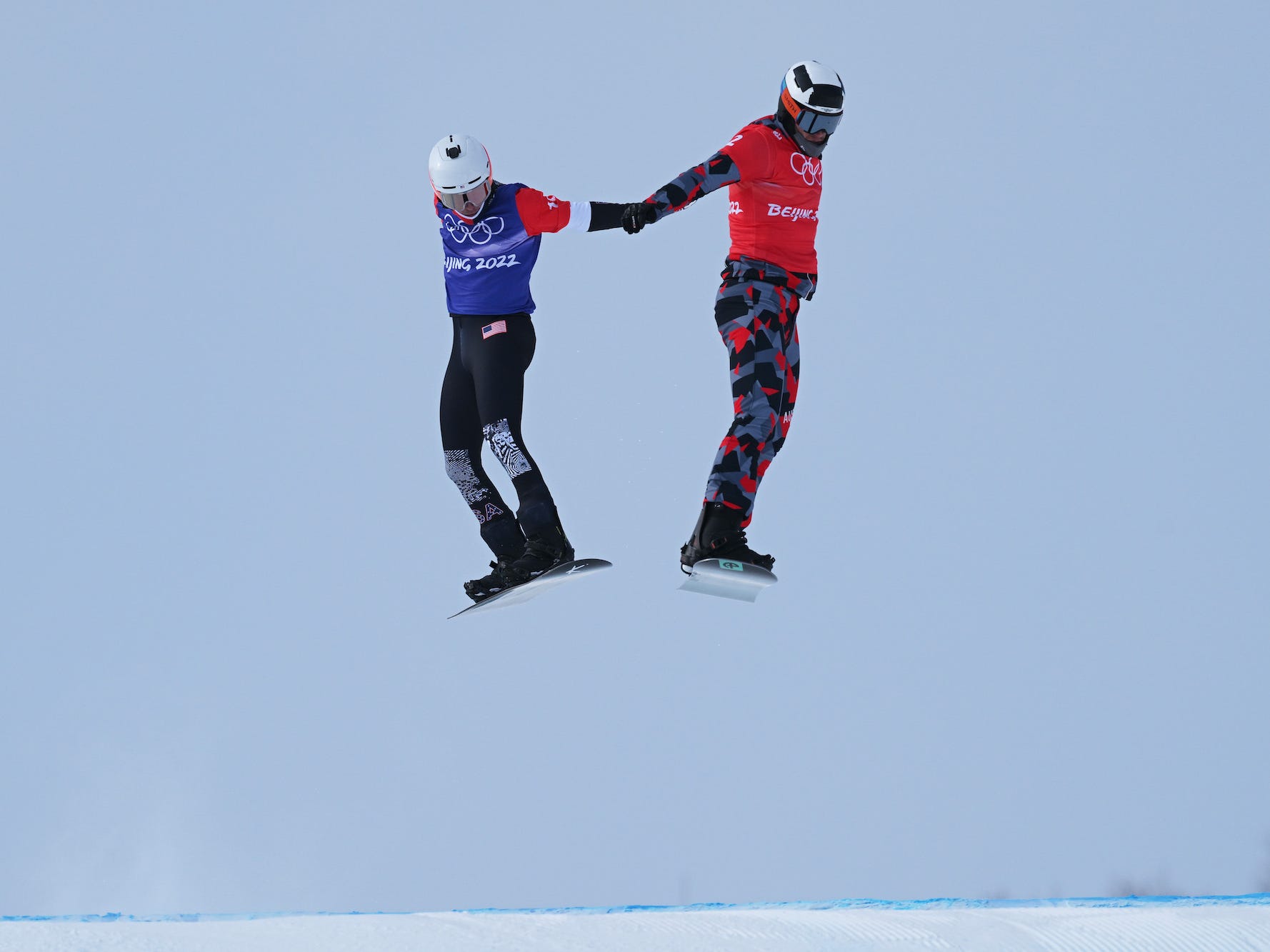Snowboarder rasen beim Snowboardcross nebeneinander in der Luft um die Wette.