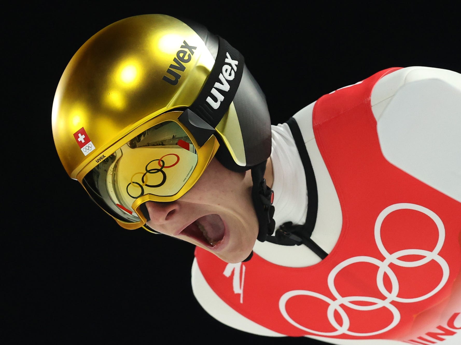 Ein Skispringer schreit, während seine Brille die olympischen Ringe reflektiert.