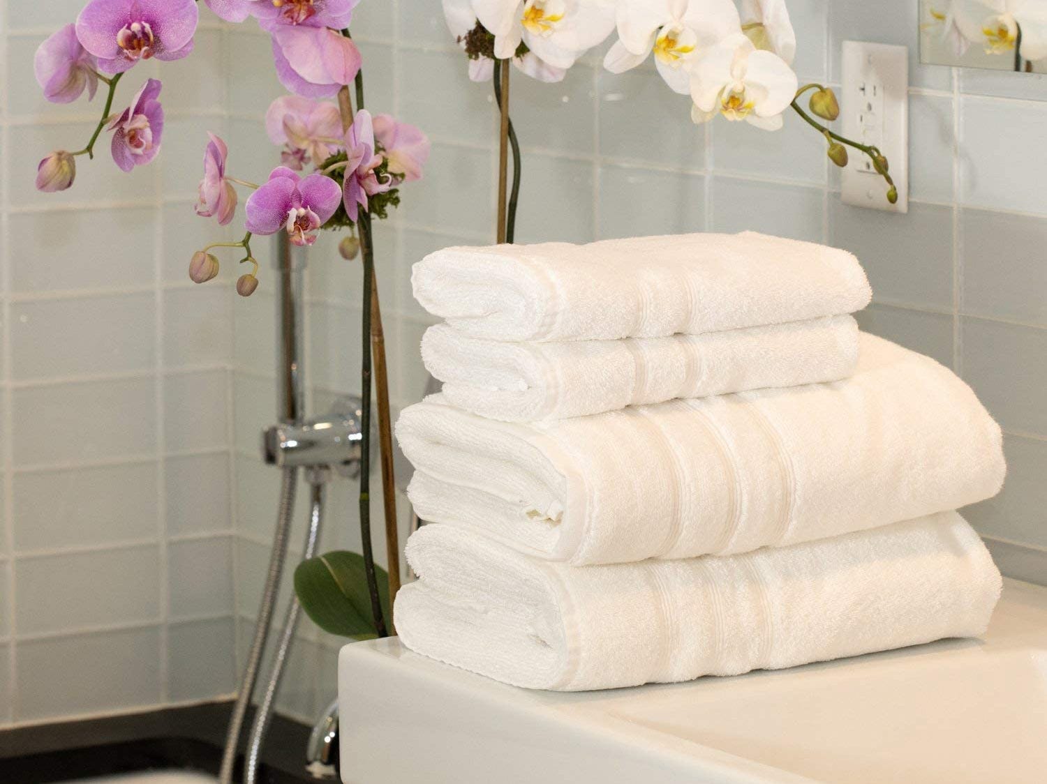 Vier weiße Frottee-Handtücher gestapelt auf Badezimmertheke mit Blumen im Hintergrund