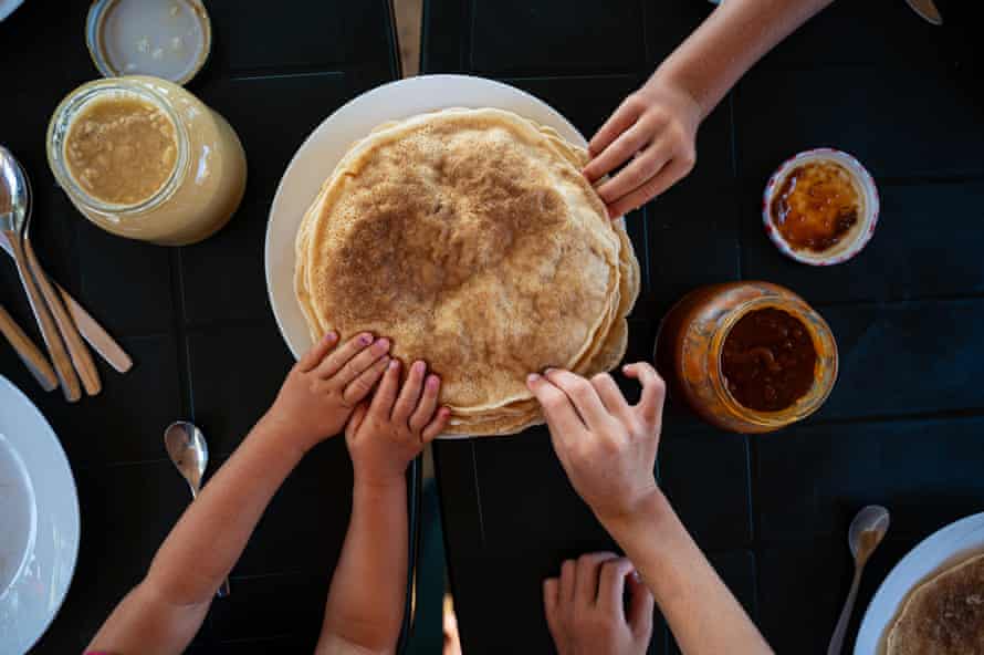 Kinder, die beim Frühstück nach Crêpes greifenDraufsicht auf Kinder, die an einem Frühstückstisch nach Crêpes greifen.
