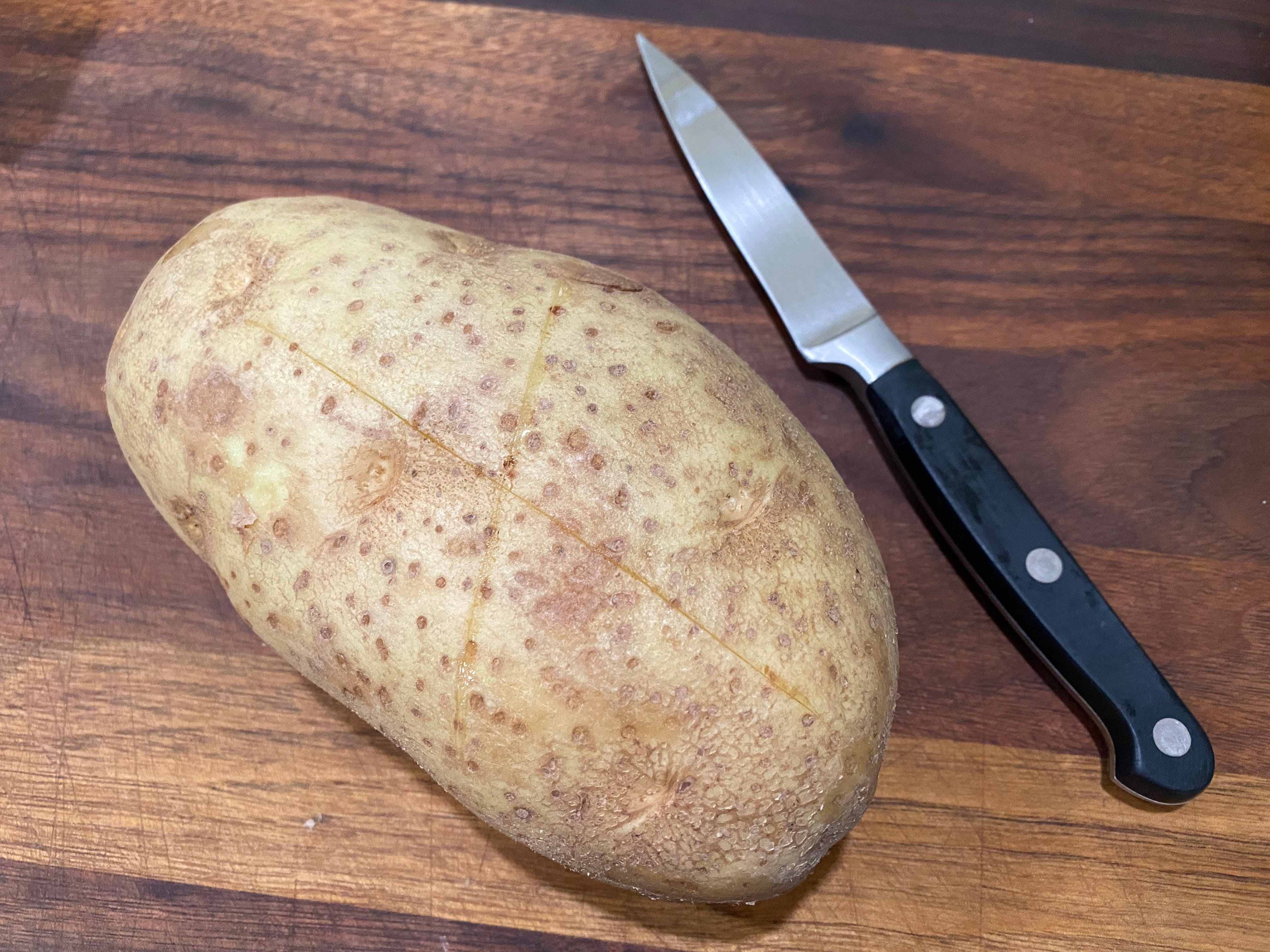 Kartoffel auf Schneidebrett neben kleinem Messer