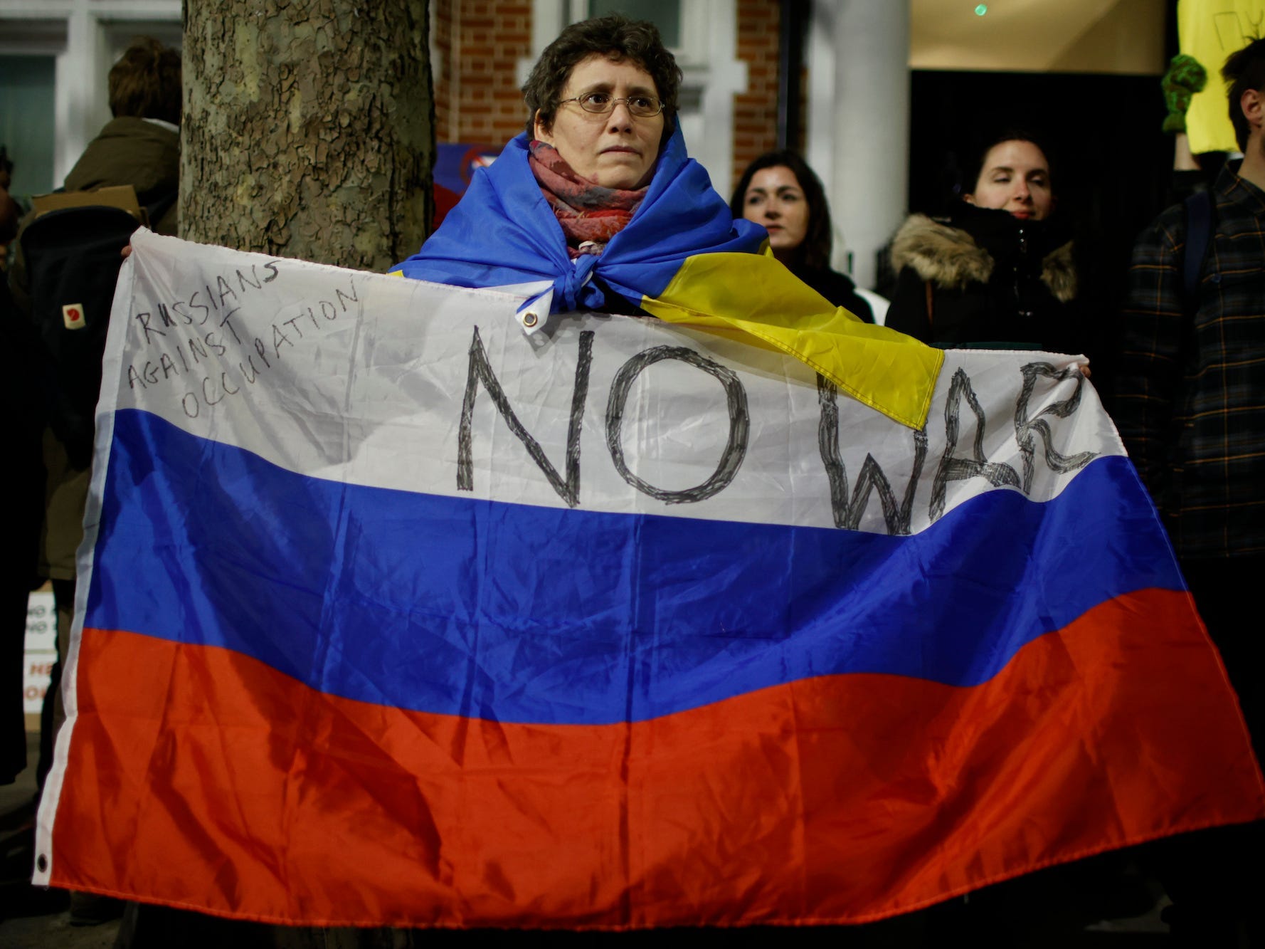 Eine Frau hält eine russische Flagge mit der Aufschrift „Russen gegen die Besatzung – kein Krieg“, während Pro-Ukraine-Aktivisten am Samstag, den 26. Februar 2022, vor der Konsularabteilung der russischen Botschaft in London protestieren.