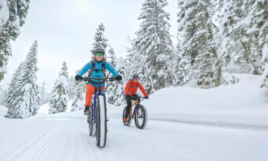 Männliche und weibliche Mountainbiker, die auf schneebedeckten Landschaften Fatbikes fahren.