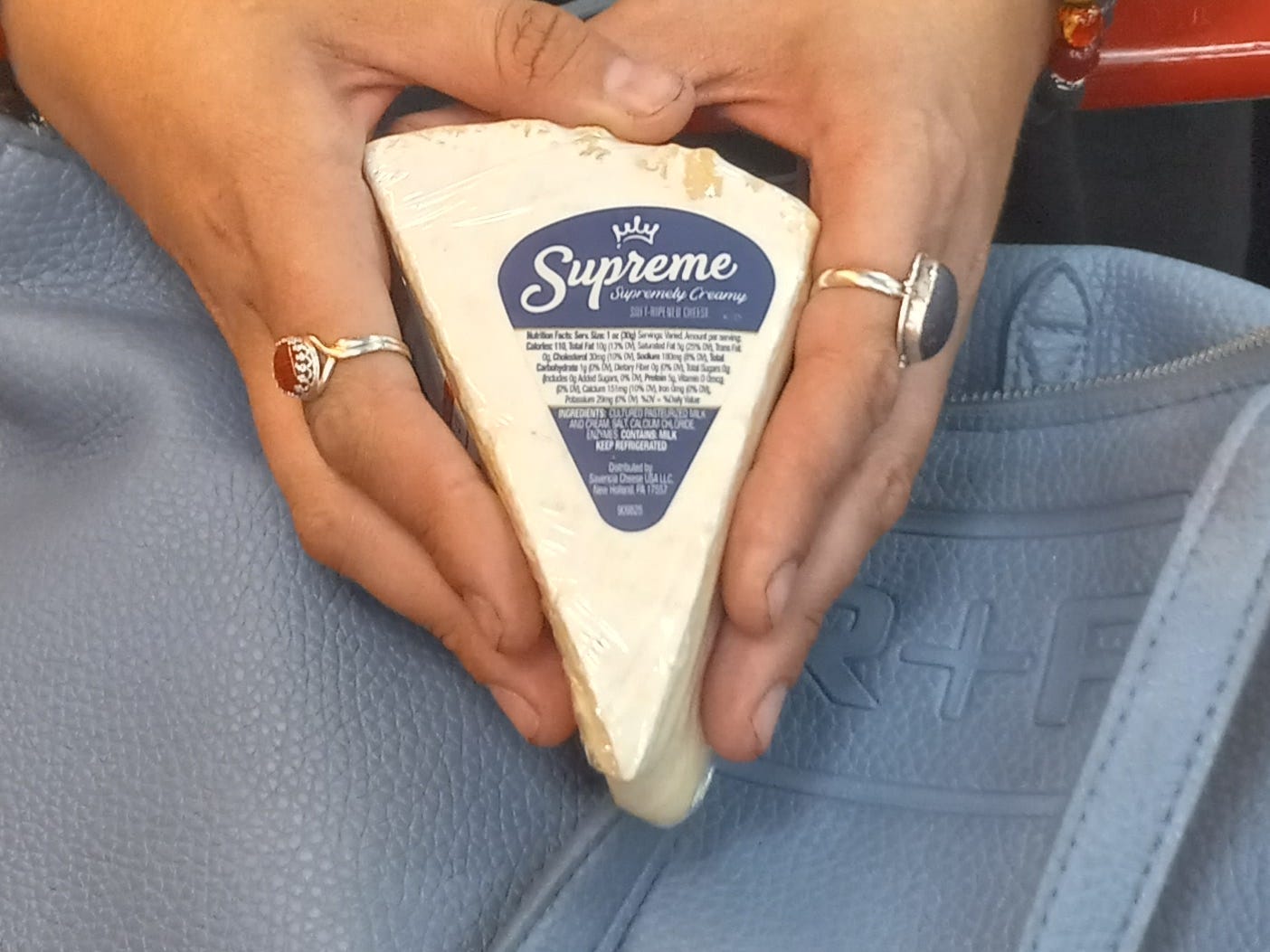 Hand hält ein Stück Brie-Käse über einem Einkaufswagen bei Trader Joe's