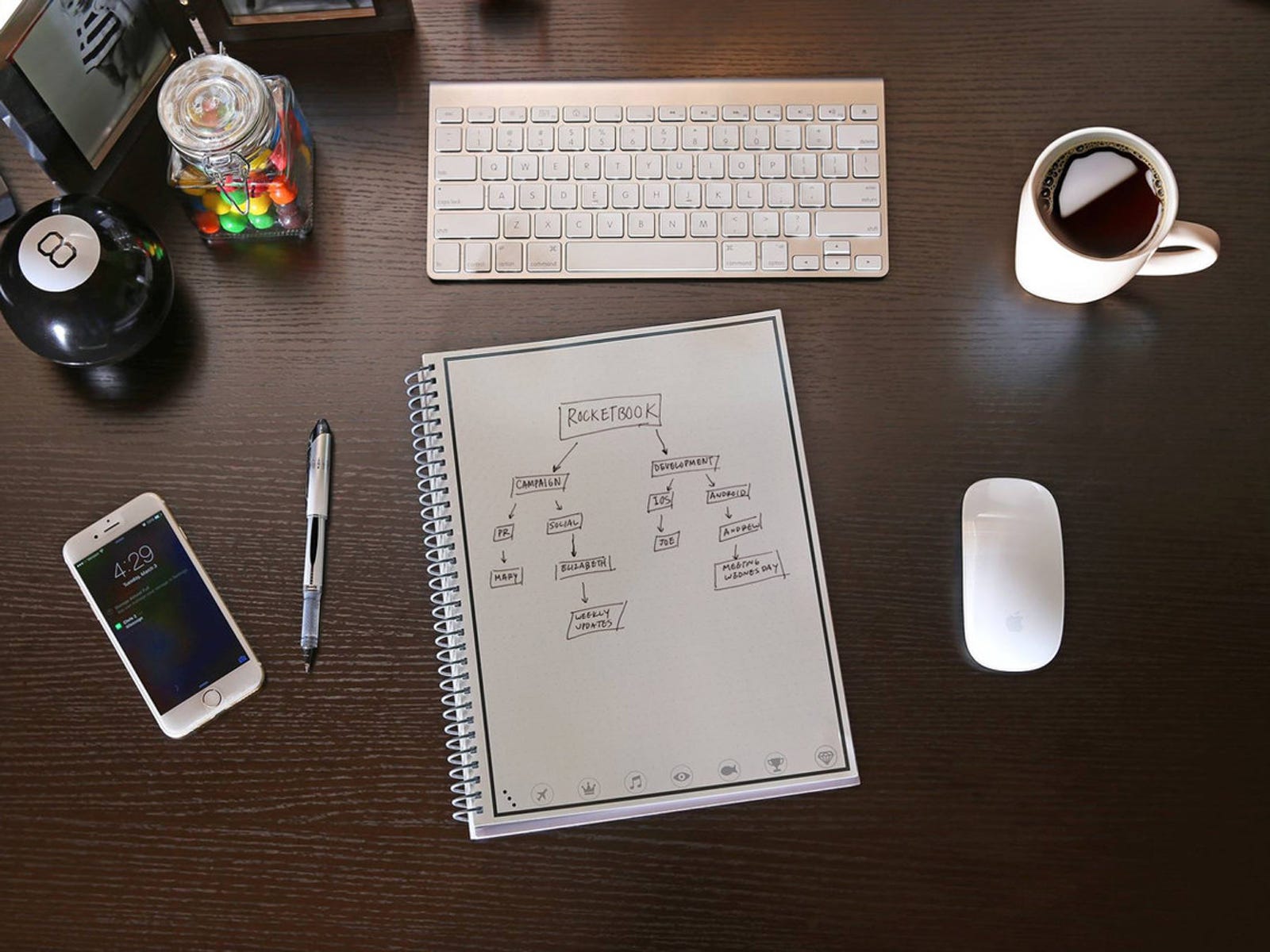 Bild eines Desktops mit Notizbuch, Tastatur, Kaffee, Maus, Telefon und Stift darauf