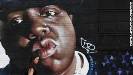 Eine Frau geht am brasilianischen Künstler Sipros vorbei.  Wandgemälde des Rappers Biggie Smalls, das am 6. Juni 2019 an einer Wand im Stadtteil Bushwick in Brooklyn, New York, zu sehen war.