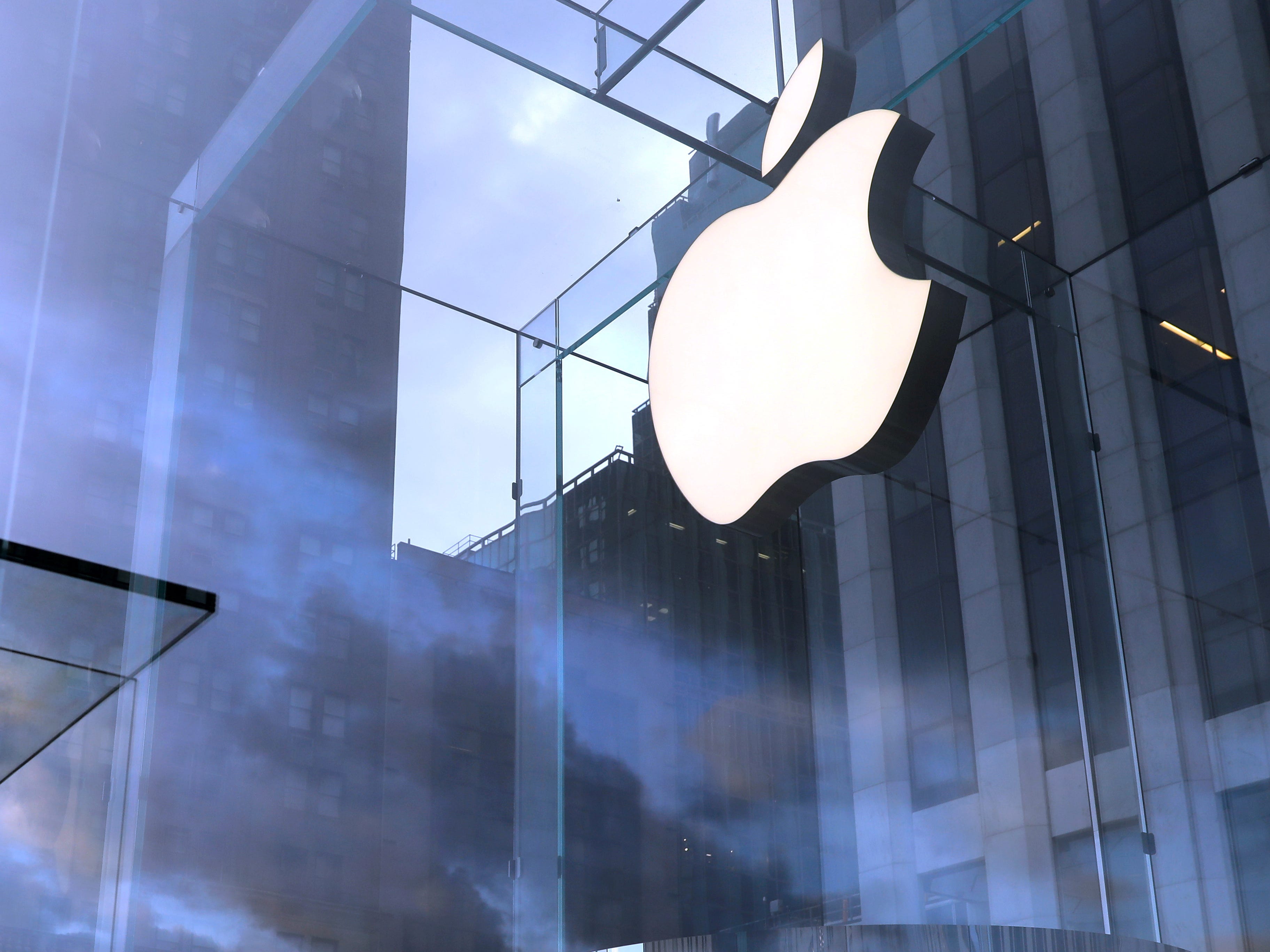 Ein bewölkter Himmel hinter einem hell erleuchteten Apple-Logo in einem Geschäft in Manhattan