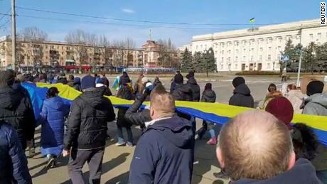 Livestream-Aufnahmen zeigen Menschen, die ein Transparent in den Farben der ukrainischen Flagge tragen, während sie am 13. März in Cherson gegen die russische Invasion in der Ukraine protestieren.