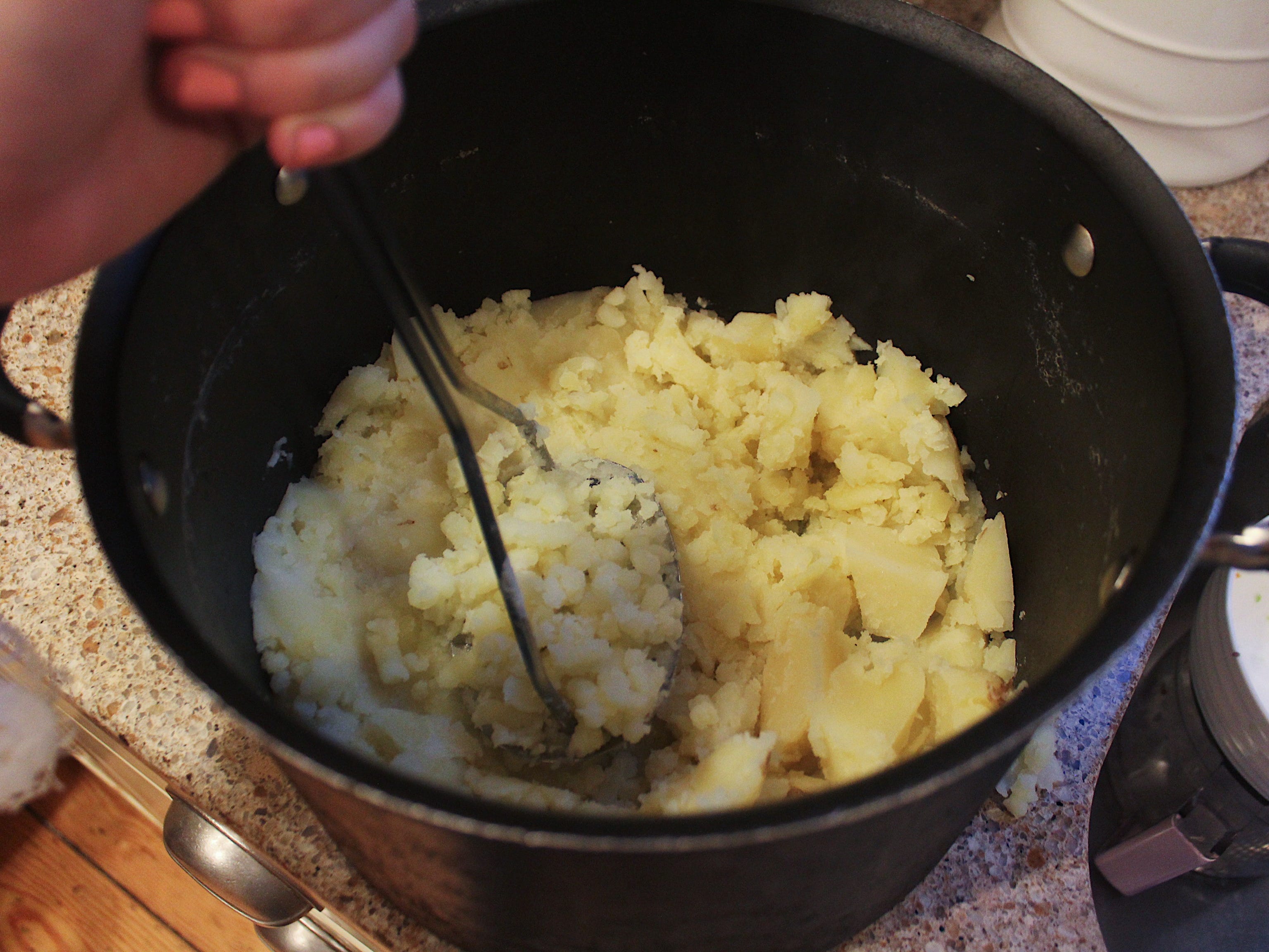 Hand Kartoffelpüree in einem schwarzen Topf