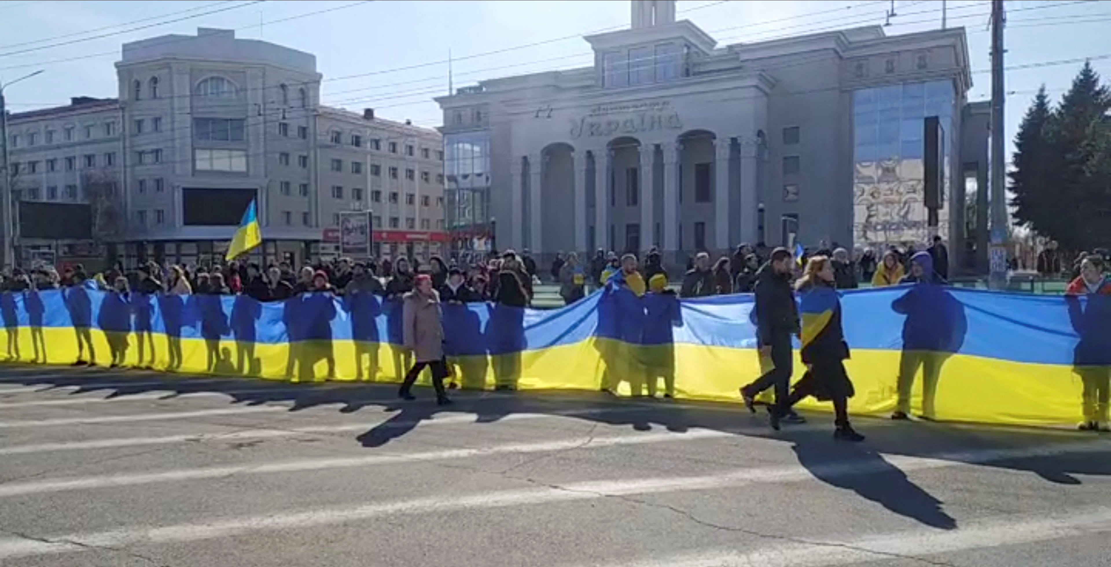 Menschen, die ein Banner in den Farben der ukrainischen Flagge halten, während sie am 13. März 2022 in Cherson, Ukraine, gegen Russlands Invasion in der Ukraine protestieren.