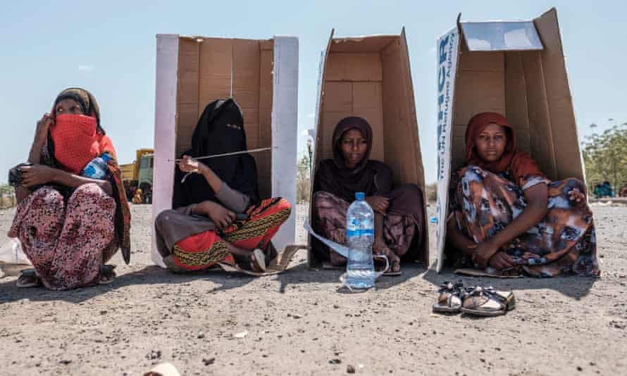 Frauen sitzen in der Sonne unter Kartons mit UN-Markenzeichen
