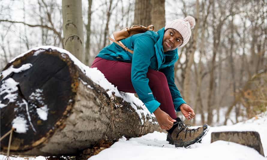 Camara Chambers sitzt auf einem gefällten Baumstamm im Schnee, um ihre Wanderschuhe anzuziehen