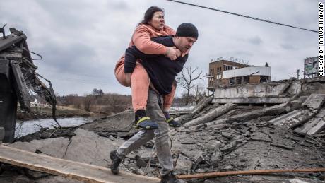 Ein Mann trägt eine Frau, als sie am Sonntag auf der Flucht aus Irpin, Ukraine, einen improvisierten Weg überqueren.