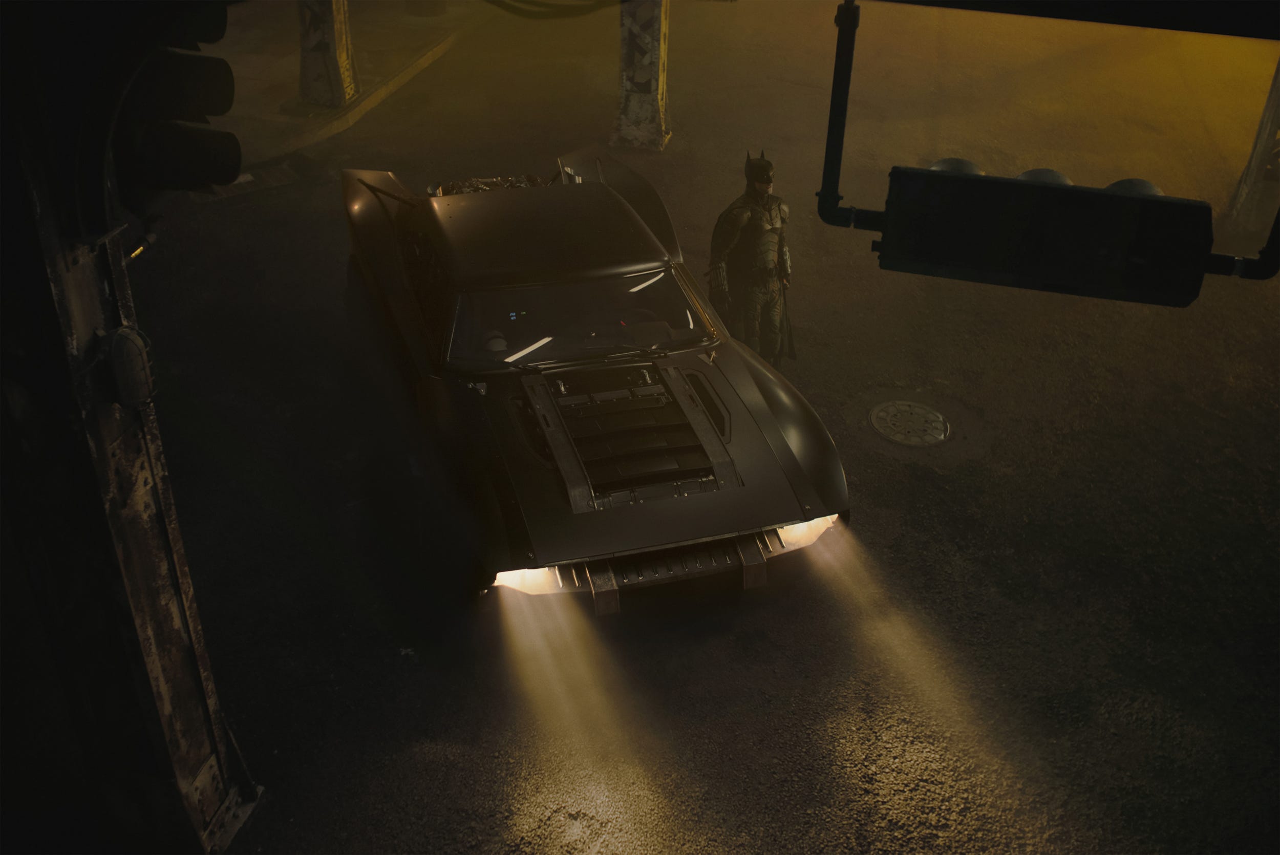 Batman steht neben dem Batmobil