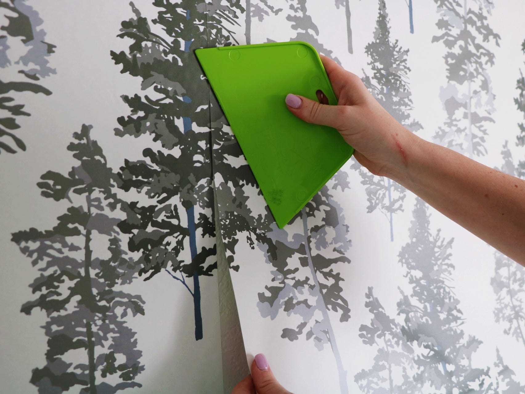Nahaufnahme der Hand mit einem Glättungswerkzeug zum Glätten von Chasing Paper Peel und Stick-Tapeten, die an einer Wand haften.