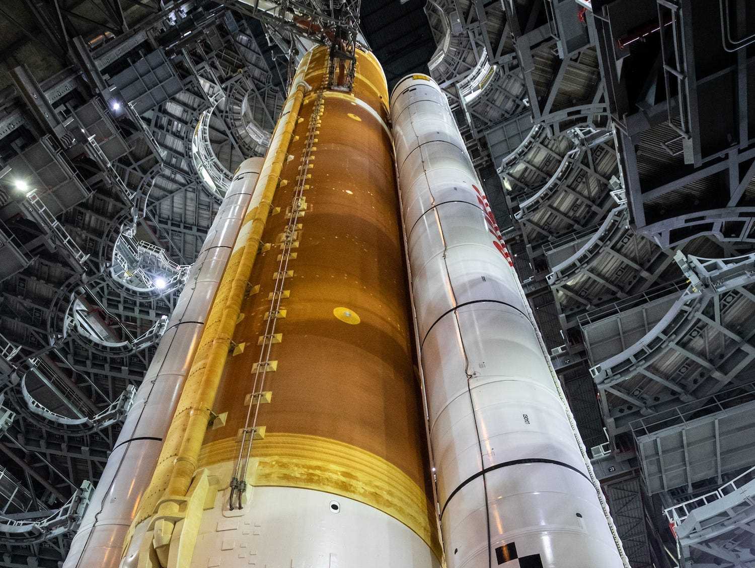 30 Stockwerke hoch ragt eine weiße und orangefarbene Rakete über drei Arbeiter der Montagehalle