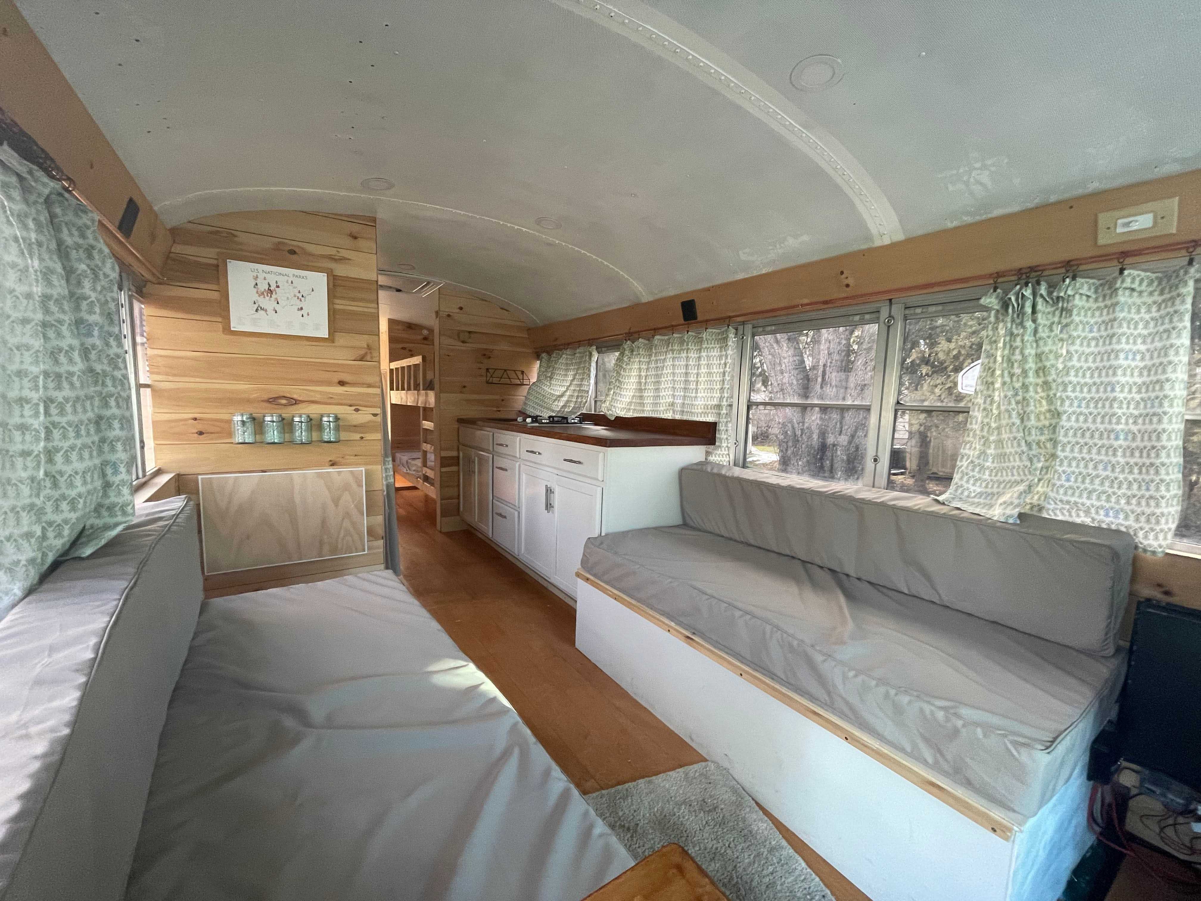 Innenraum eines neu gestalteten Busses mit grauen Sitzen, Holzvertäfelung, grünen Vorhängen und weißer Decke