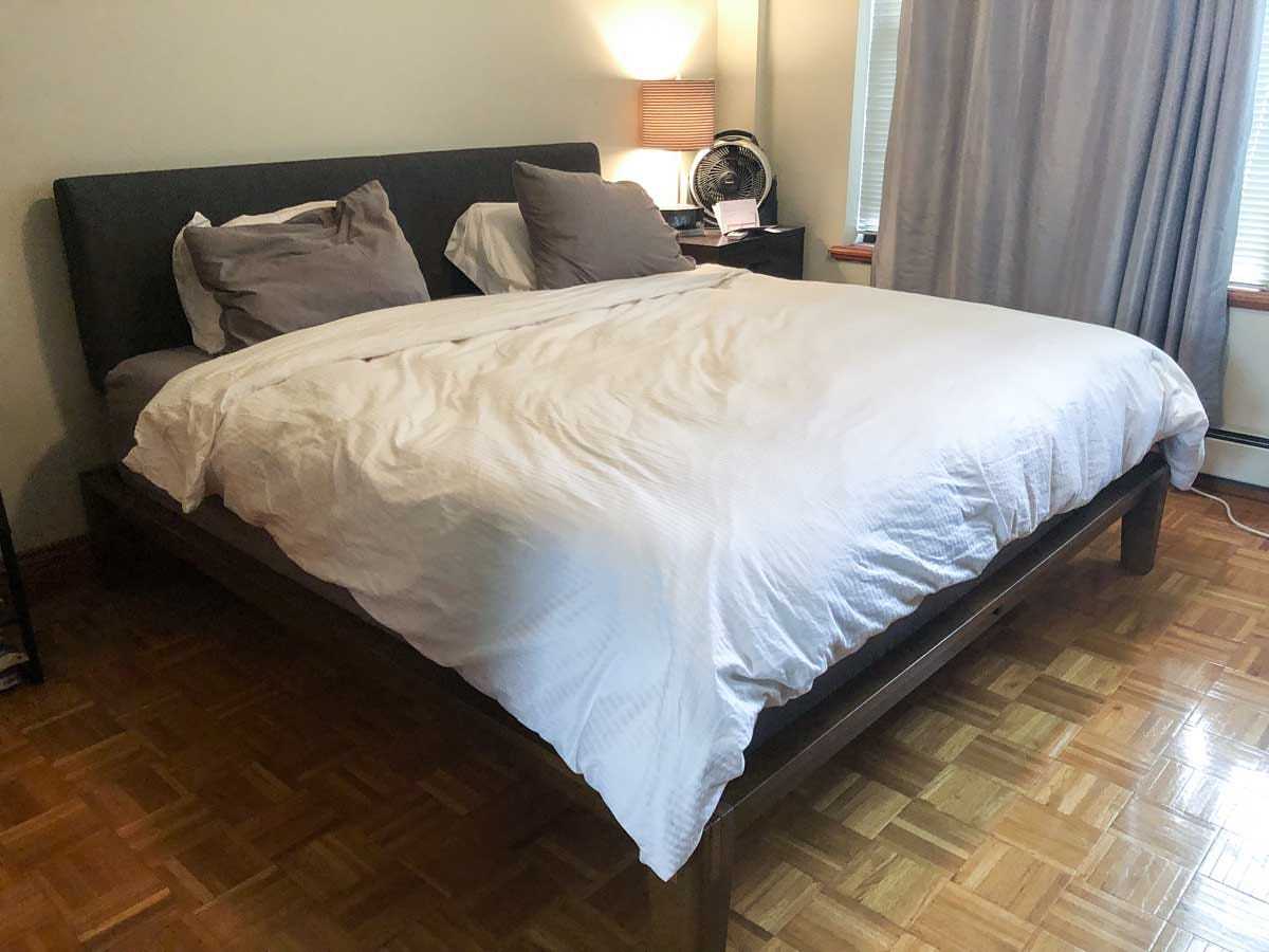 Das montierte Thuma Bettgestell aus Holz mit darauf liegender Matratze und ein fertig bezogenes Bett.