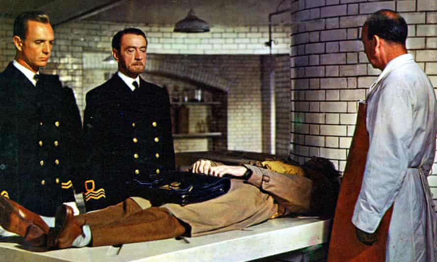 Zwei Männer in Militäruniform und ein Arzt im weißen Kittel betrachten den Leichnam eines Mannes auf einer Steinplatte