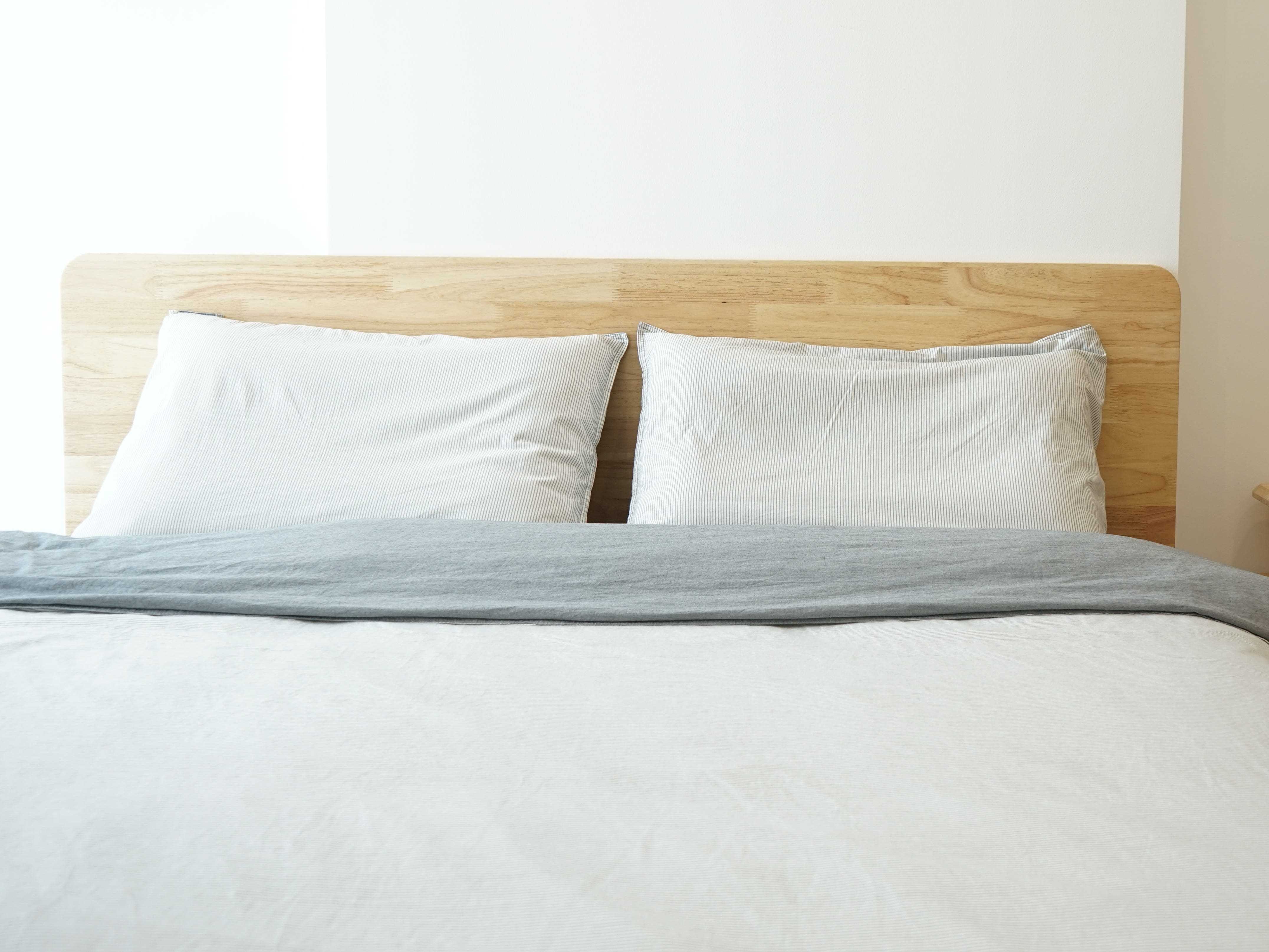 Bett mit Kopfteil aus Holz, weißen Kissen und weißen Laken mit Beistelltisch aus Holz und Pflanze darauf