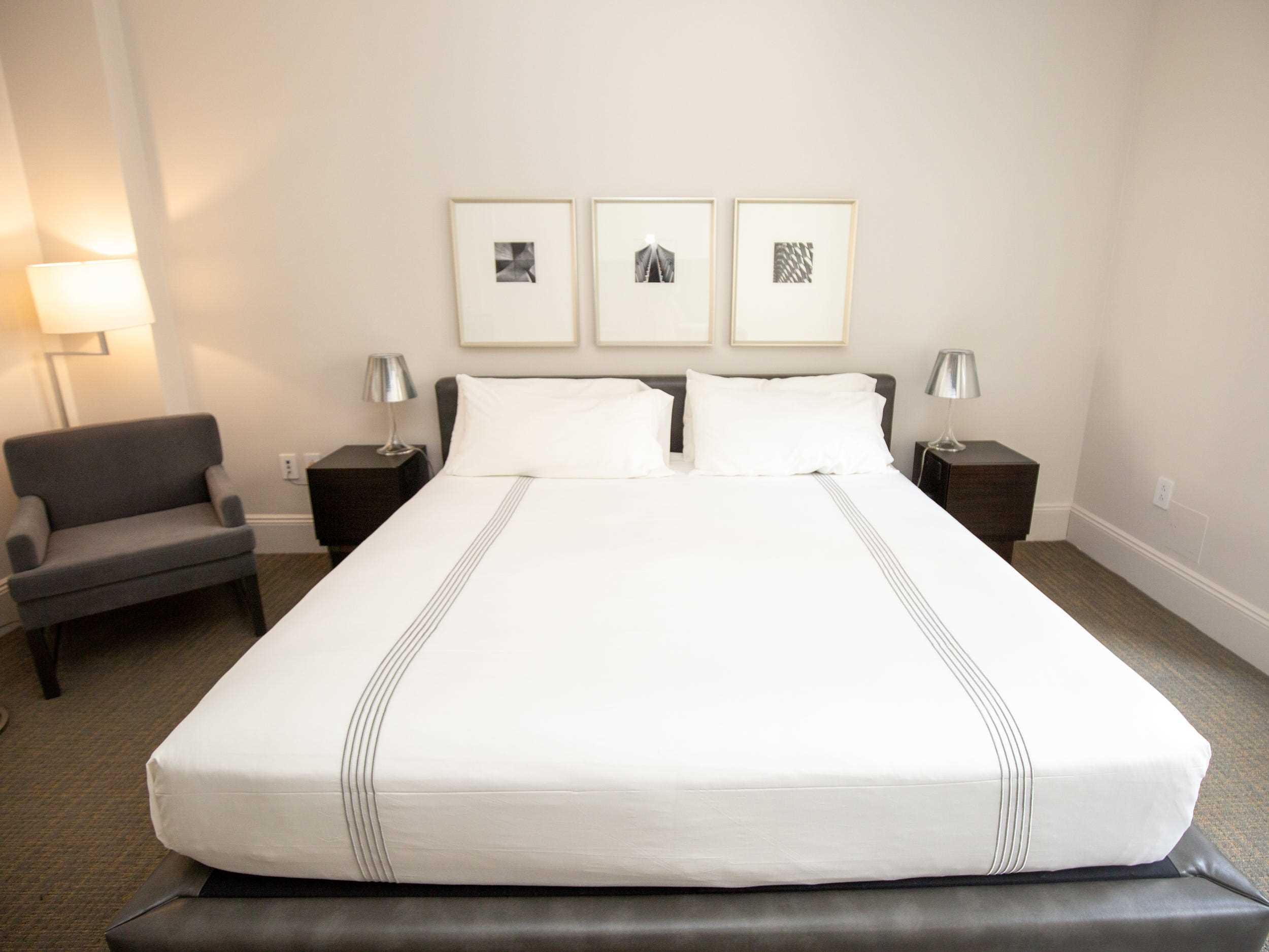 Wandkunst über einem Bett mit zwei Nachttischen.  In der Ecke des Zimmers steht ein Liegestuhl.