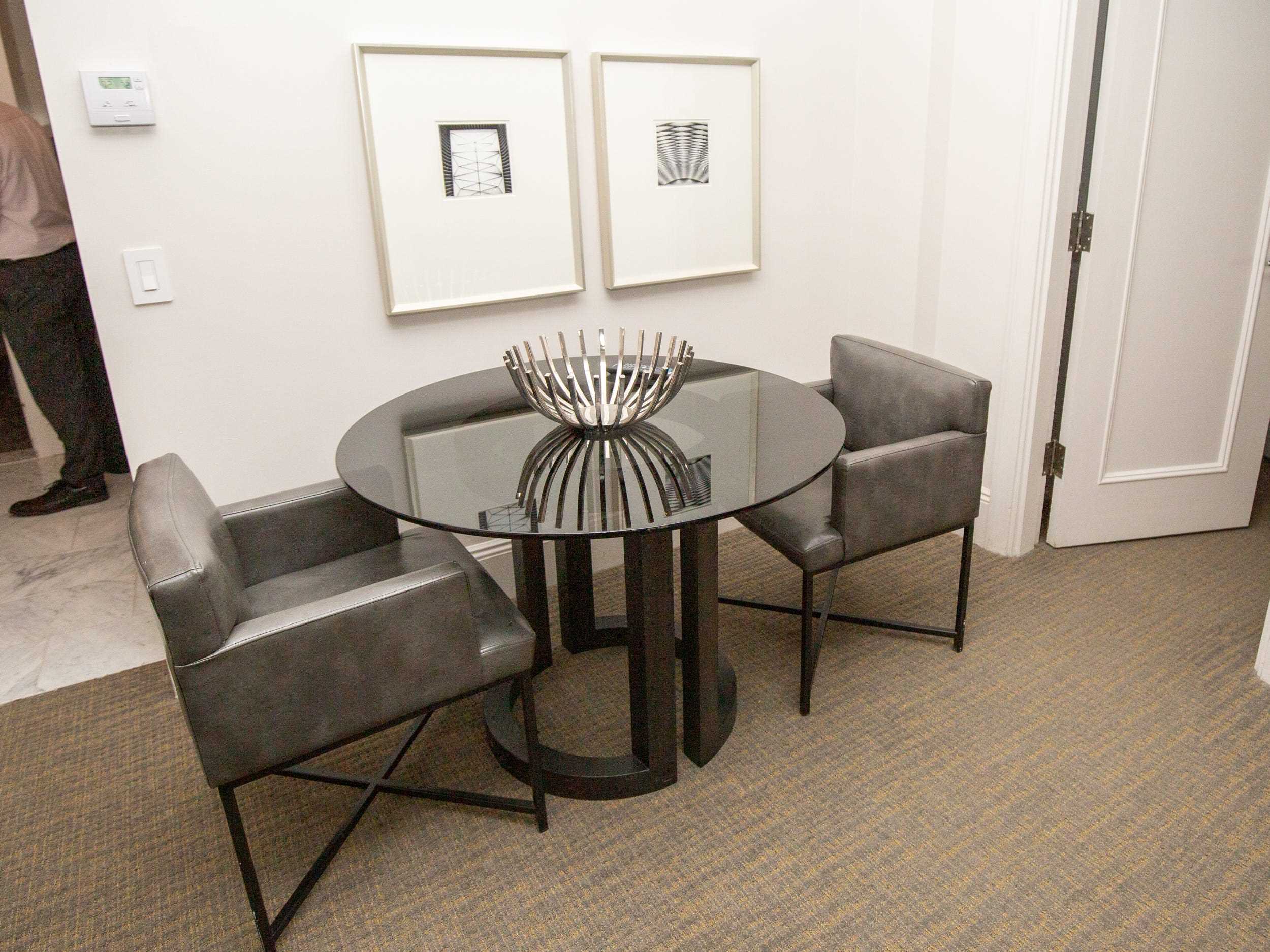 Ein runder Tisch mit zwei Stühlen und zwei an der Wand hängenden Drucken.