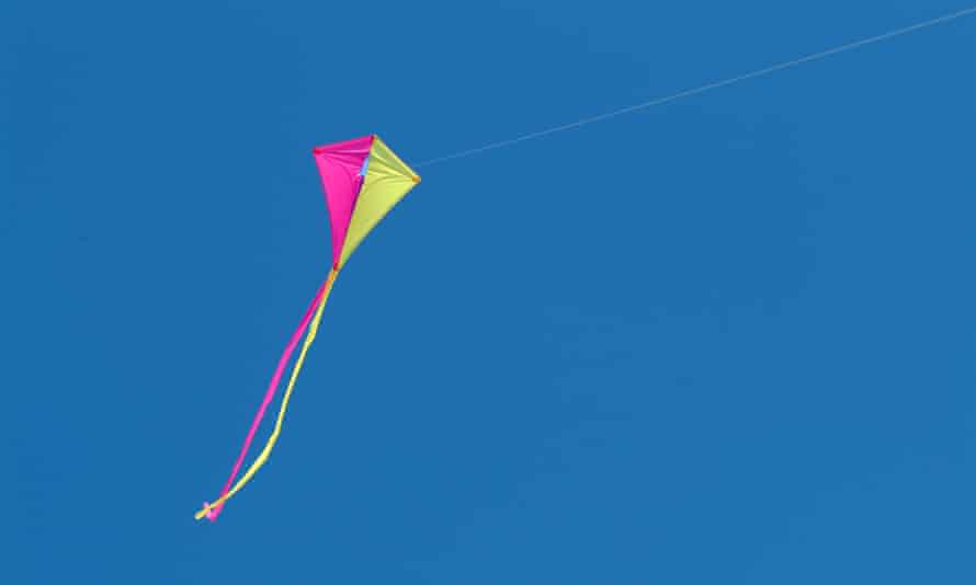 Ein rosa und gelber Drachen fliegt gegen einen blauen Himmel, an dem zwei lange Bänder hängen. 
