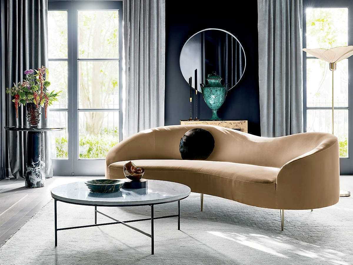 Die CB2 Curvo Camel Couch sitzt in einem dunkel gestrichenen Wohnzimmer mit anderen Möbeln.
