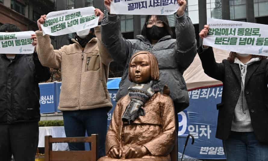 Südkoreanische Demonstranten halten im März 2021 Transparente neben einer Statue eines Teenagers hoch, die „Trostfrauen“ symbolisiert, in der Nähe der japanischen Botschaft in Seoul