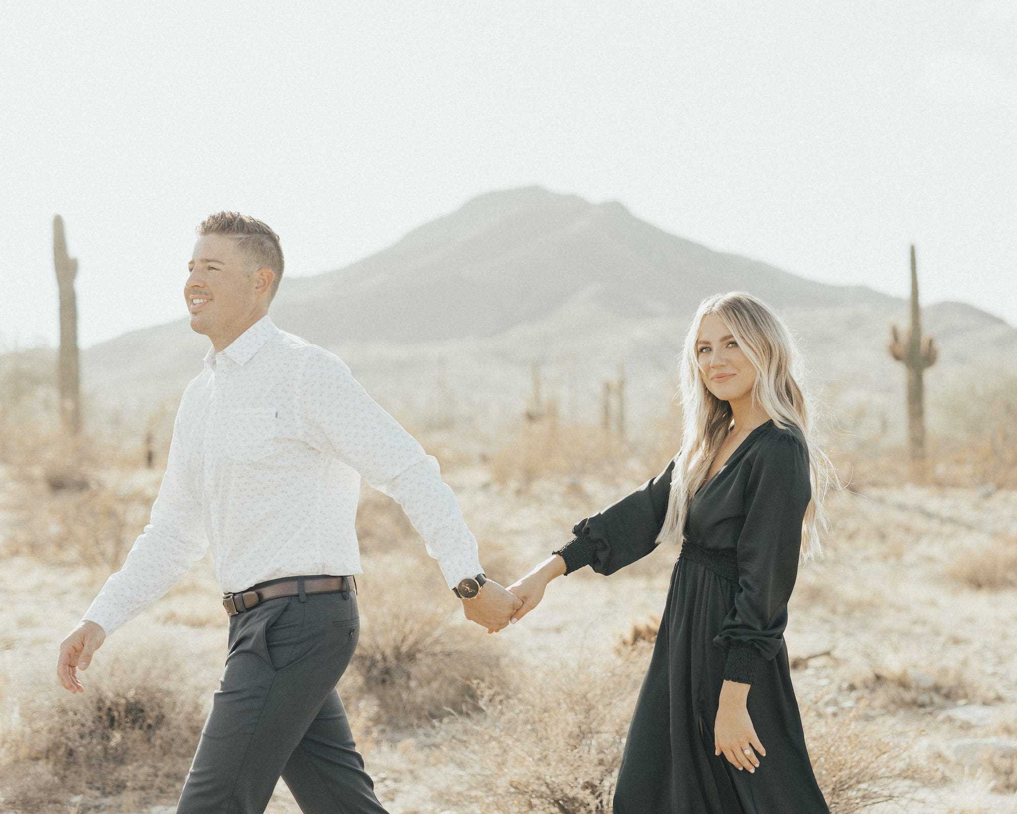 Ein Mann und eine Frau halten sich an den Händen und gehen links vom Rahmen in die Wüste.