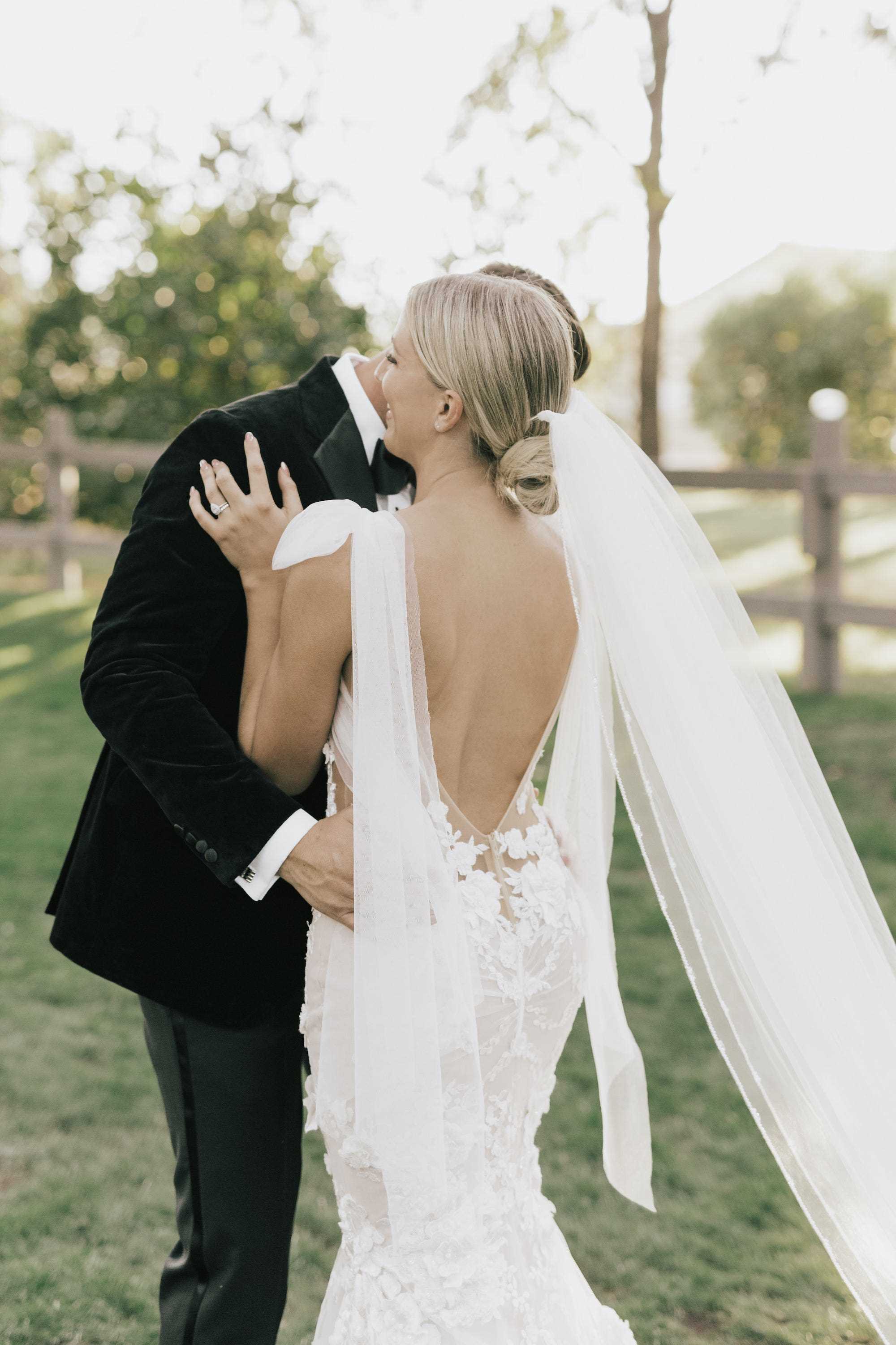 Eine Braut umarmt ihren Bräutigam und zeigt ihr rückenfreies Hochzeitskleid.