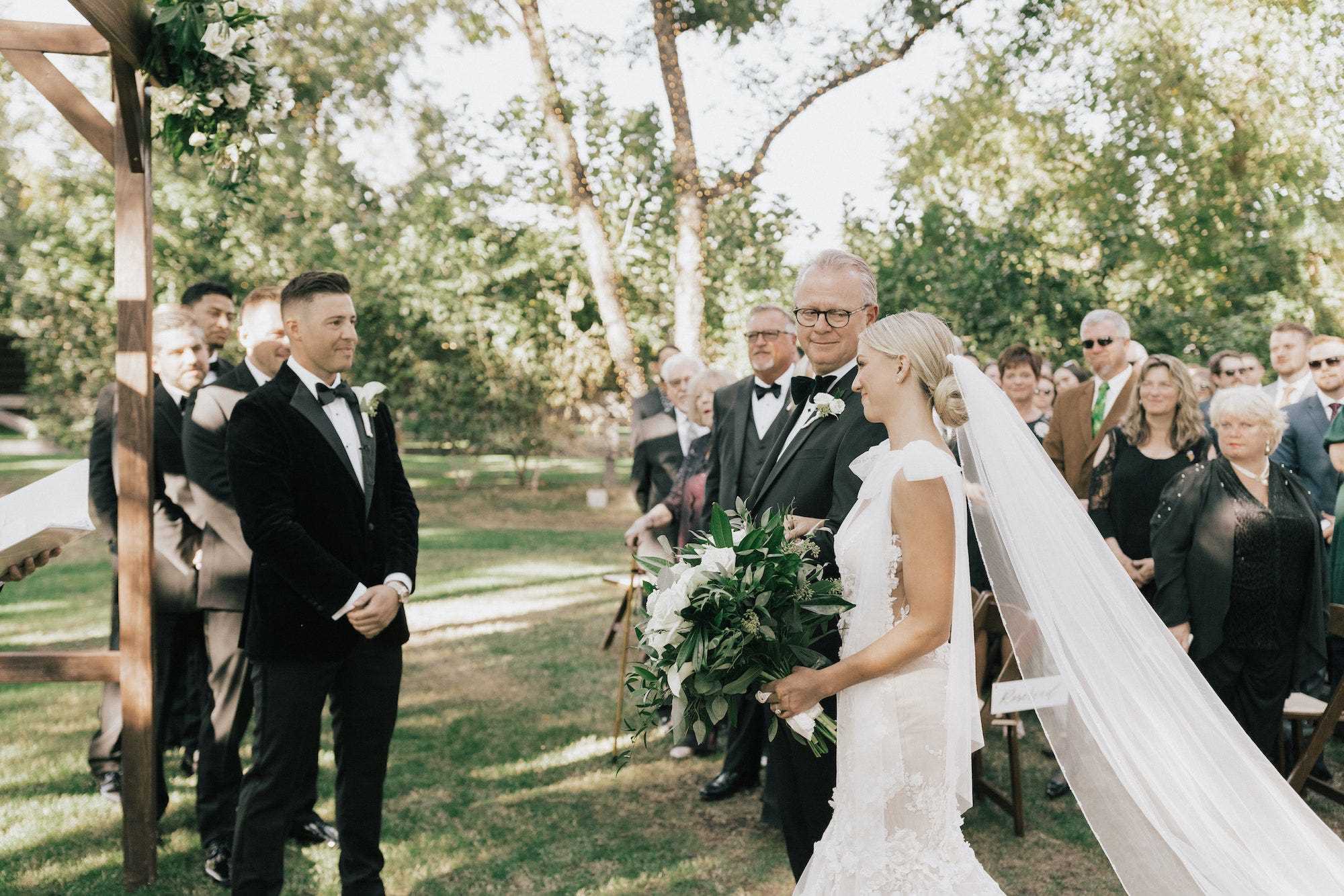 Eine Braut und ihr Vater gehen während ihrer Hochzeit im Freien auf ihren Bräutigam zu.