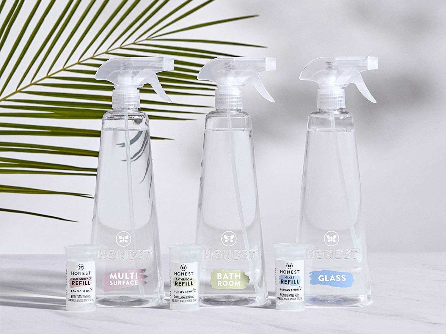 Drei Flaschen Reiniger von Honest Company stehen auf einer weißen Fläche mit einer grünen Pflanze im Hintergrund, die besten natürlichen Reinigungsprodukte im Jahr 2022.