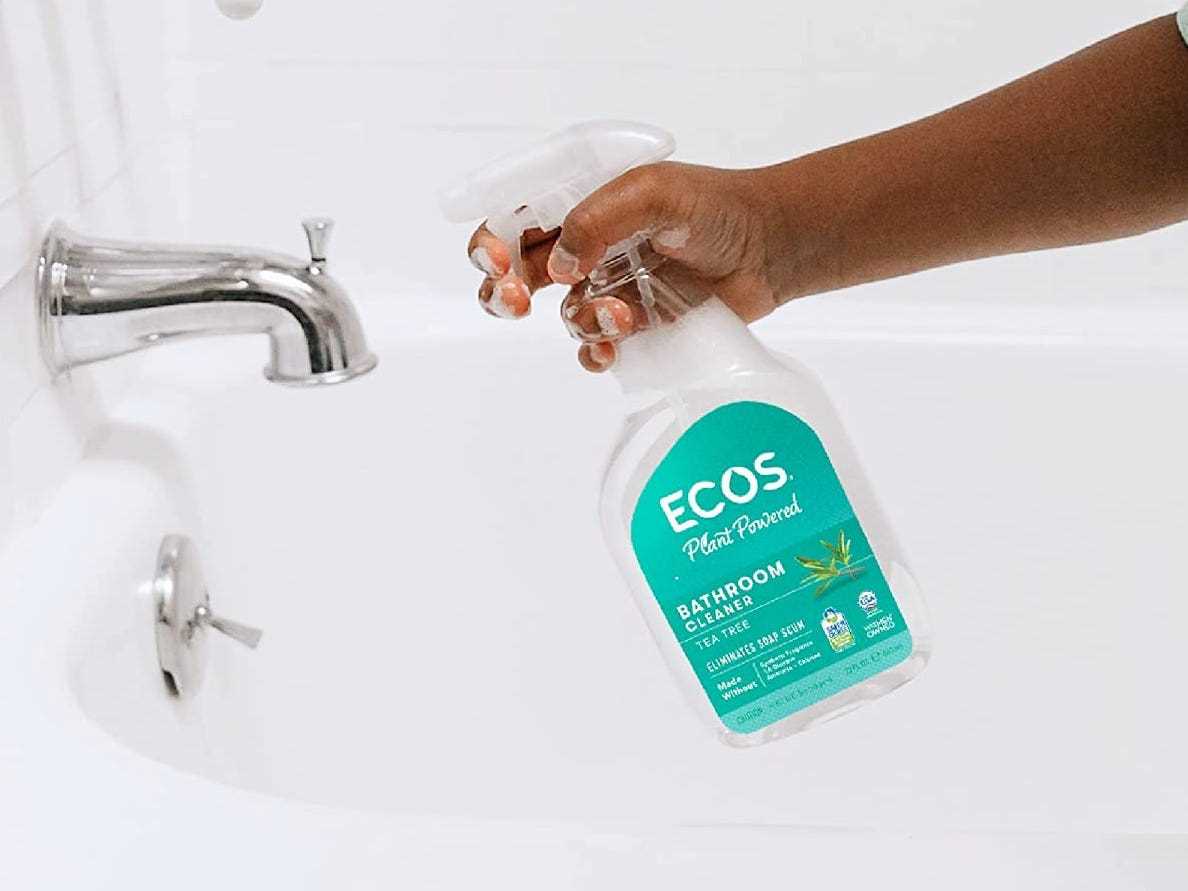 Eine Hand hält eine Flasche ECOS-Reinigungsspray in der Nähe einer Badewanne, die besten natürlichen Reinigungsprodukte im Jahr 2022.