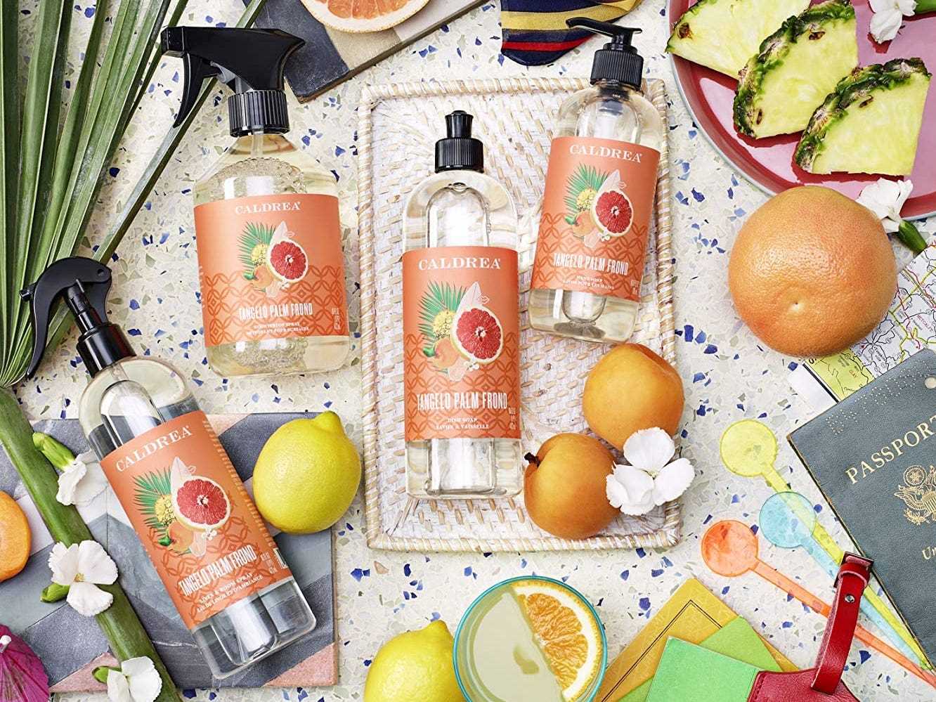 Vier Flaschen Caldera-Reiniger liegen neben Orangen, einem Reisepass und anderen Gegenständen, den besten natürlichen Reinigungsprodukten im Jahr 2022.