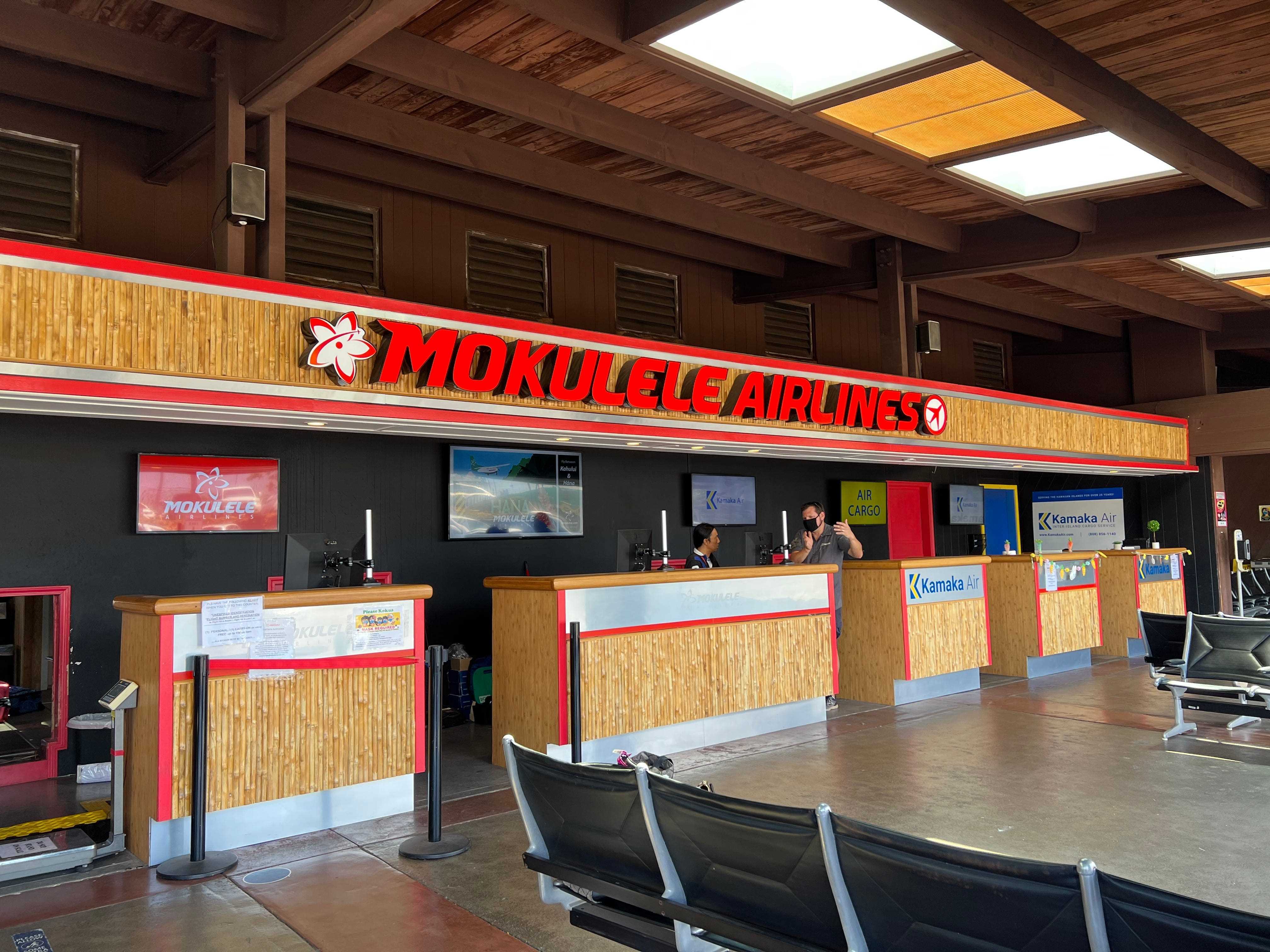 Der Check-in-Schalter bei Mokulele Airlines mit Holzschaltern und einem roten Leuchtschild