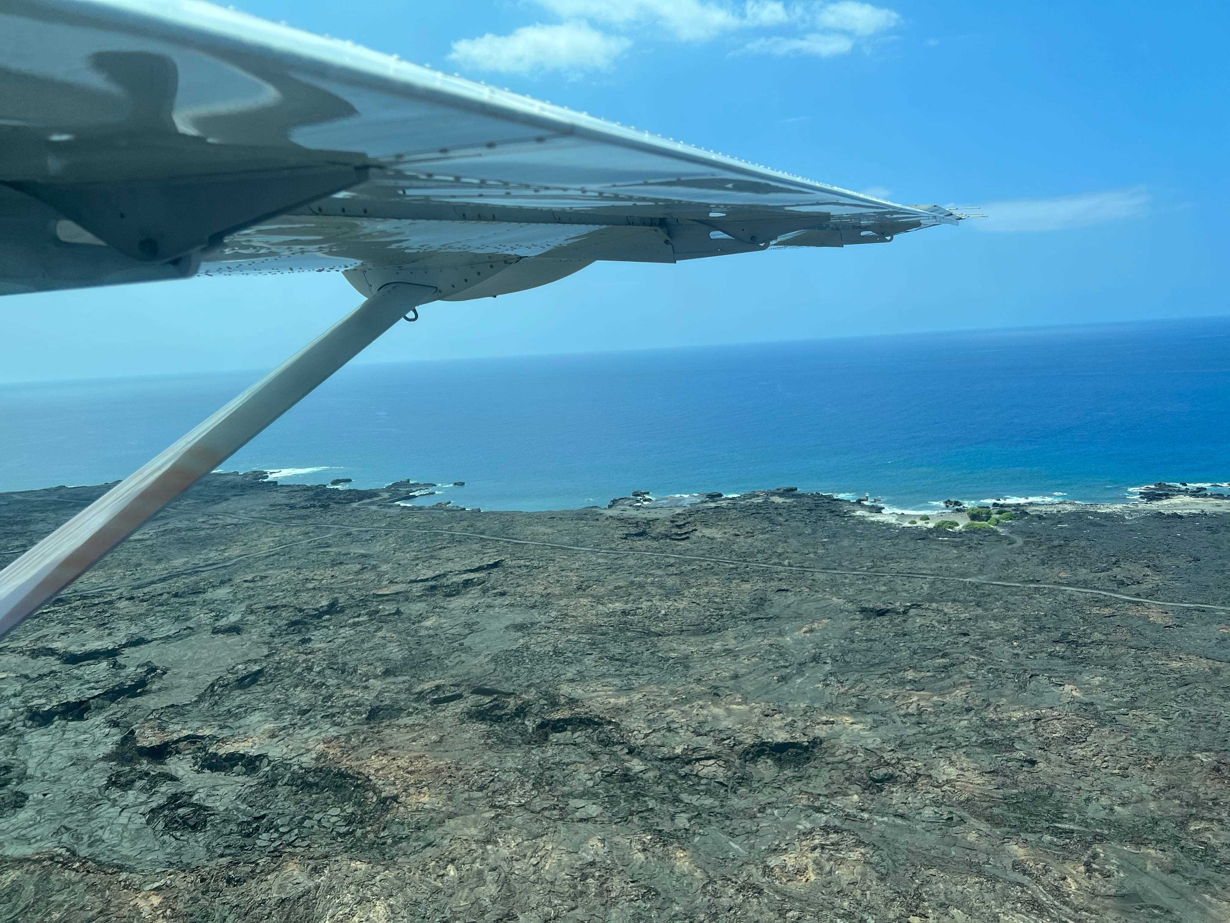 Blick auf bräunlichen Sand und Felsen mit der Flugzeugtragfläche darüber.
