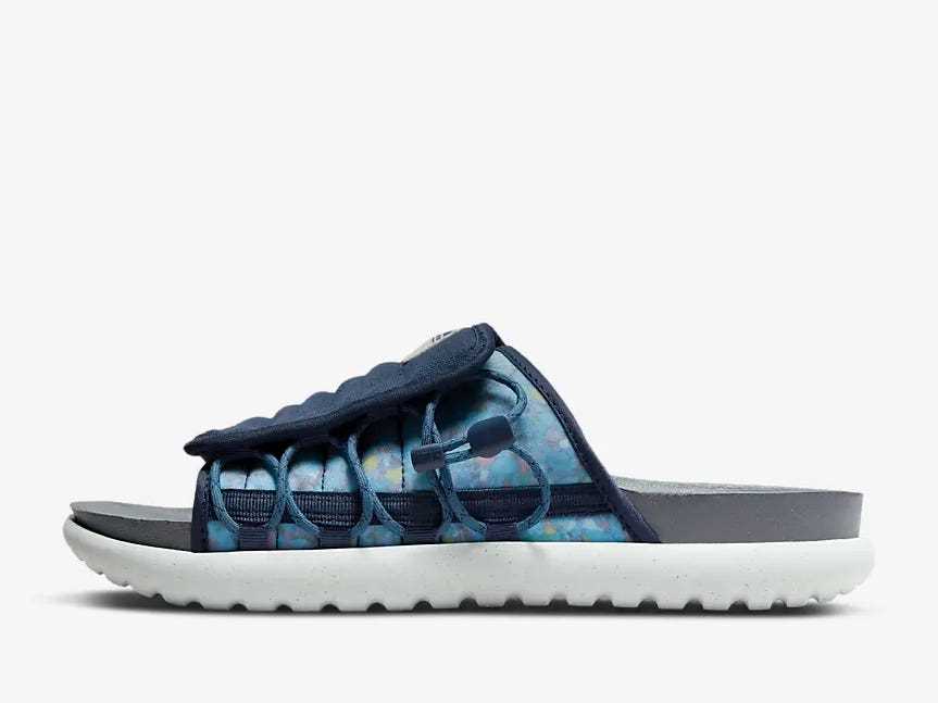 Nike Asuna 2 Next Natur.  Die Sohle der Rutsche ist grau und die Unterseite des Schuhs ist weiß.  Der obere Teil der Rutsche ist marineblau und ein hellblauer Aquarelldruck mit gemischten Farben.