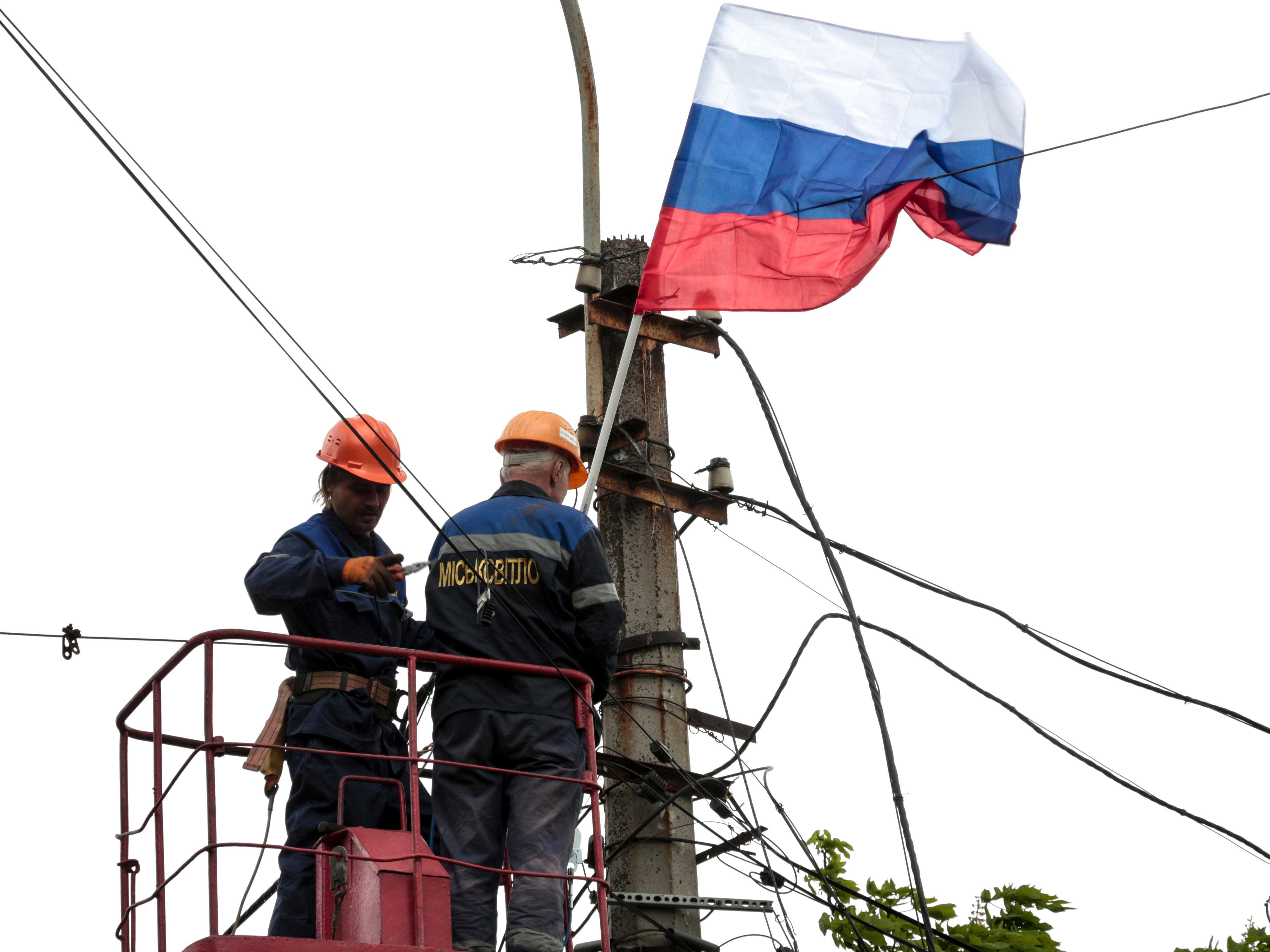 Kommunalarbeiter installieren eine russische Flagge an einem Mast.
