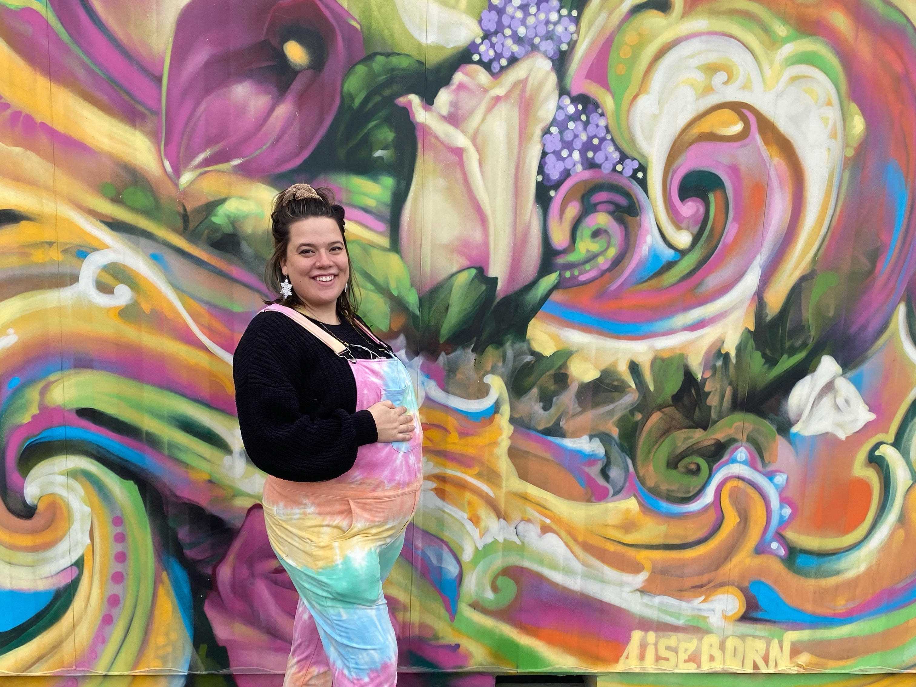 Der Schriftsteller im Batik-Overall posiert vor einem farbenfrohen Wandgemälde