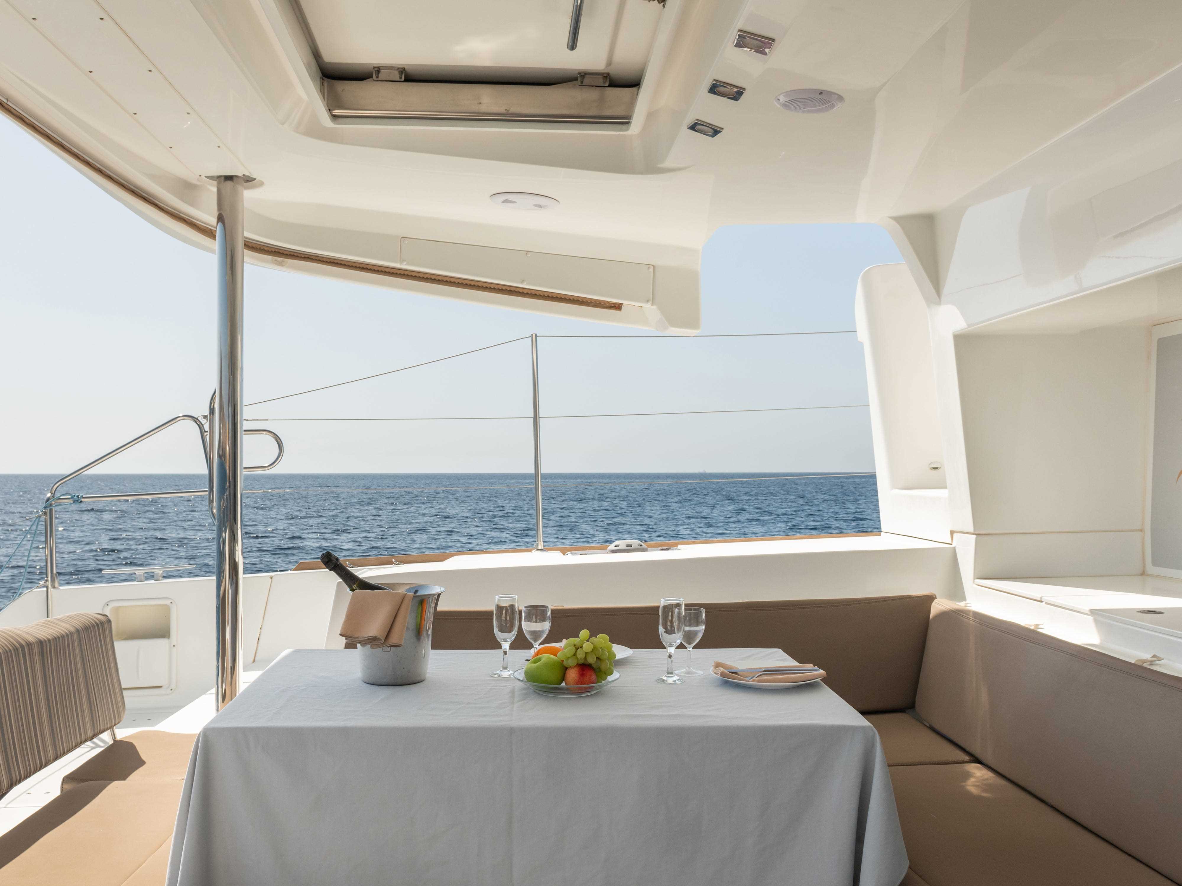 Champagner, Gläser und eine Schale mit Weintrauben auf einem Tisch mit weißer Tischdecke auf einem Schiff mit grauer Bestuhlung und Blick aufs Wasser