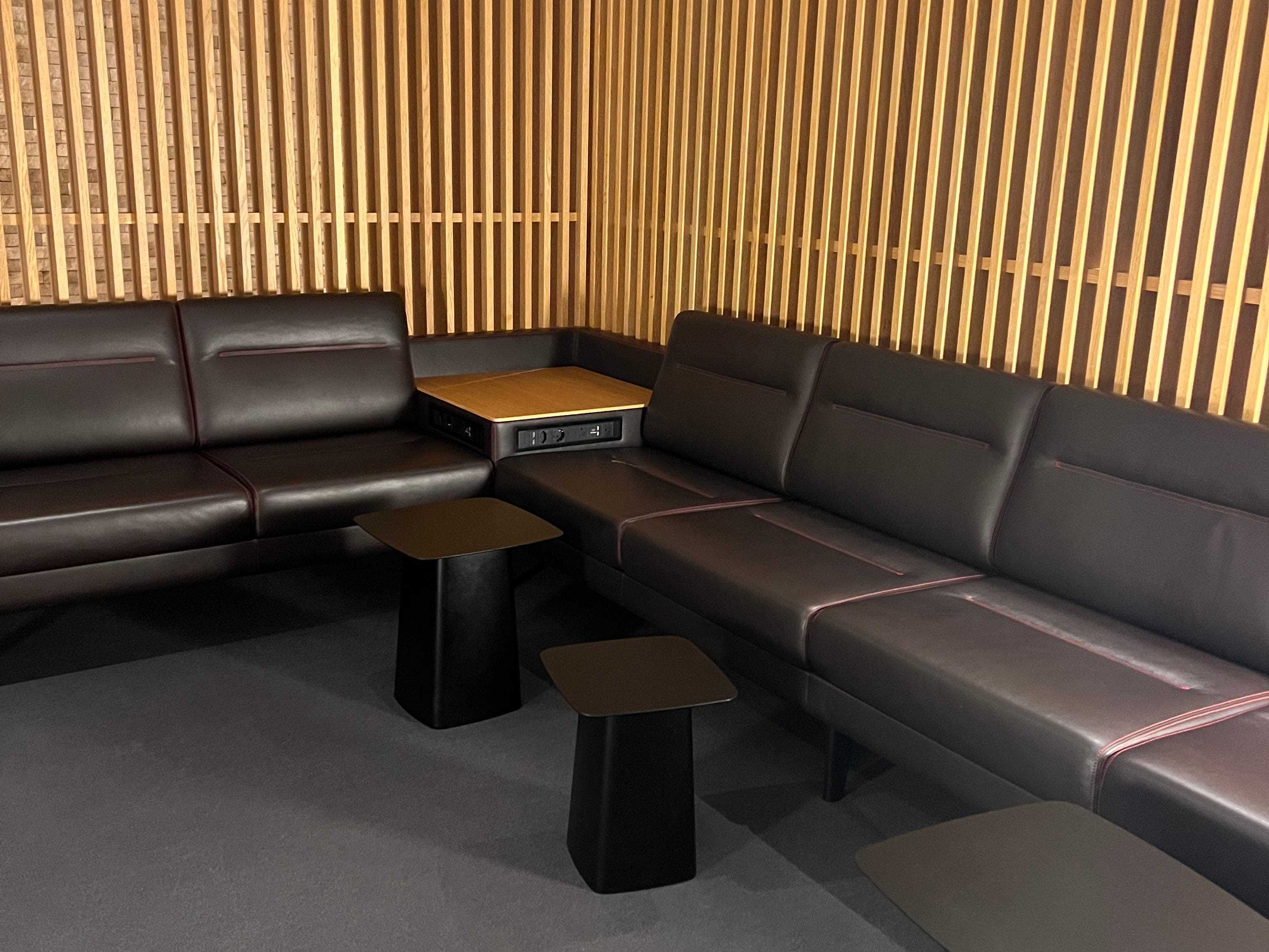 eine Flughafenlounge mit eleganten schwarzen Sofas, kleinen Tischen und einer Wand aus Holzpaneelen