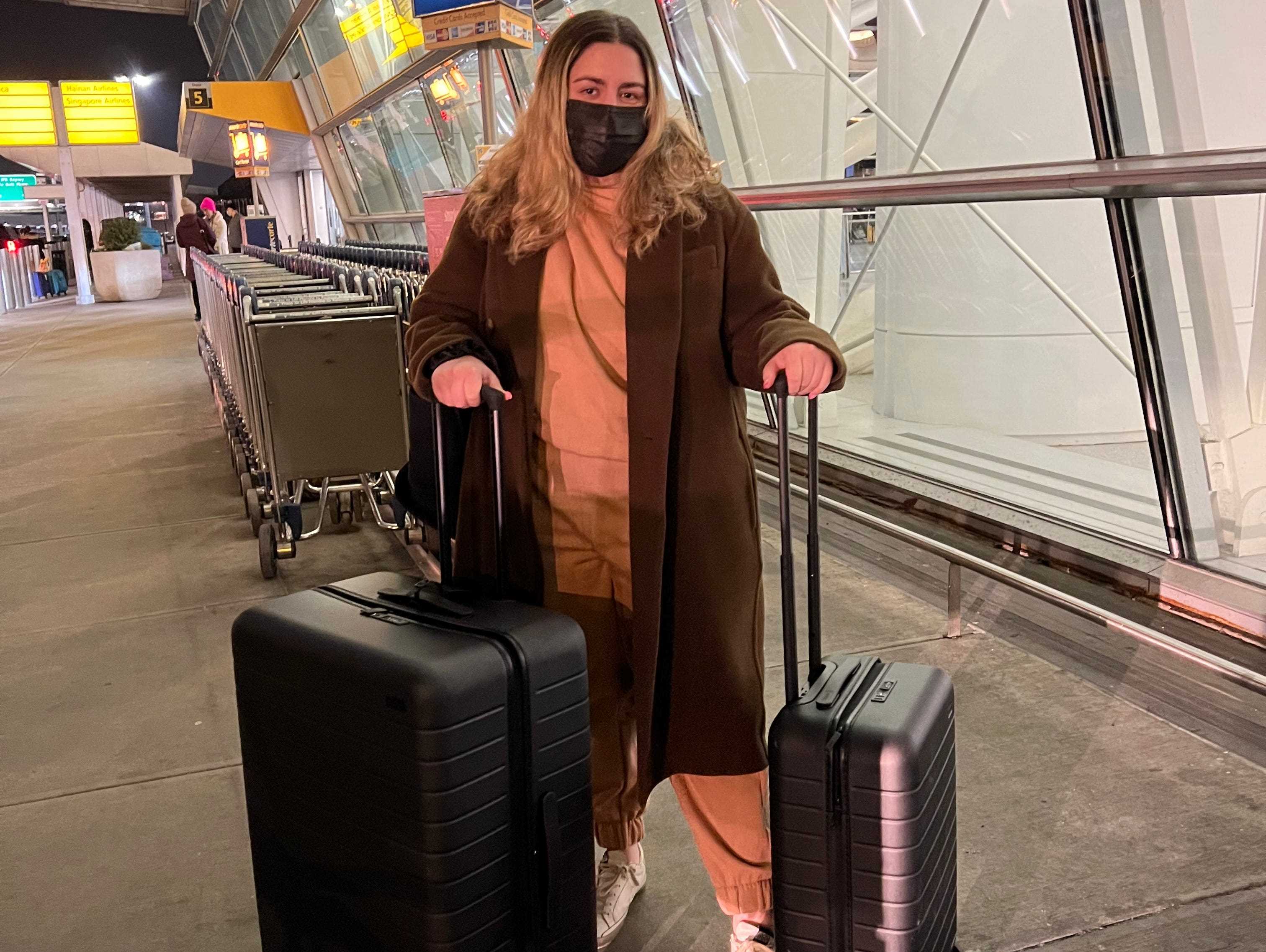 Die Schriftstellerin mit zwei Koffern und einer Maske auf dem Weg zum Flughafen.