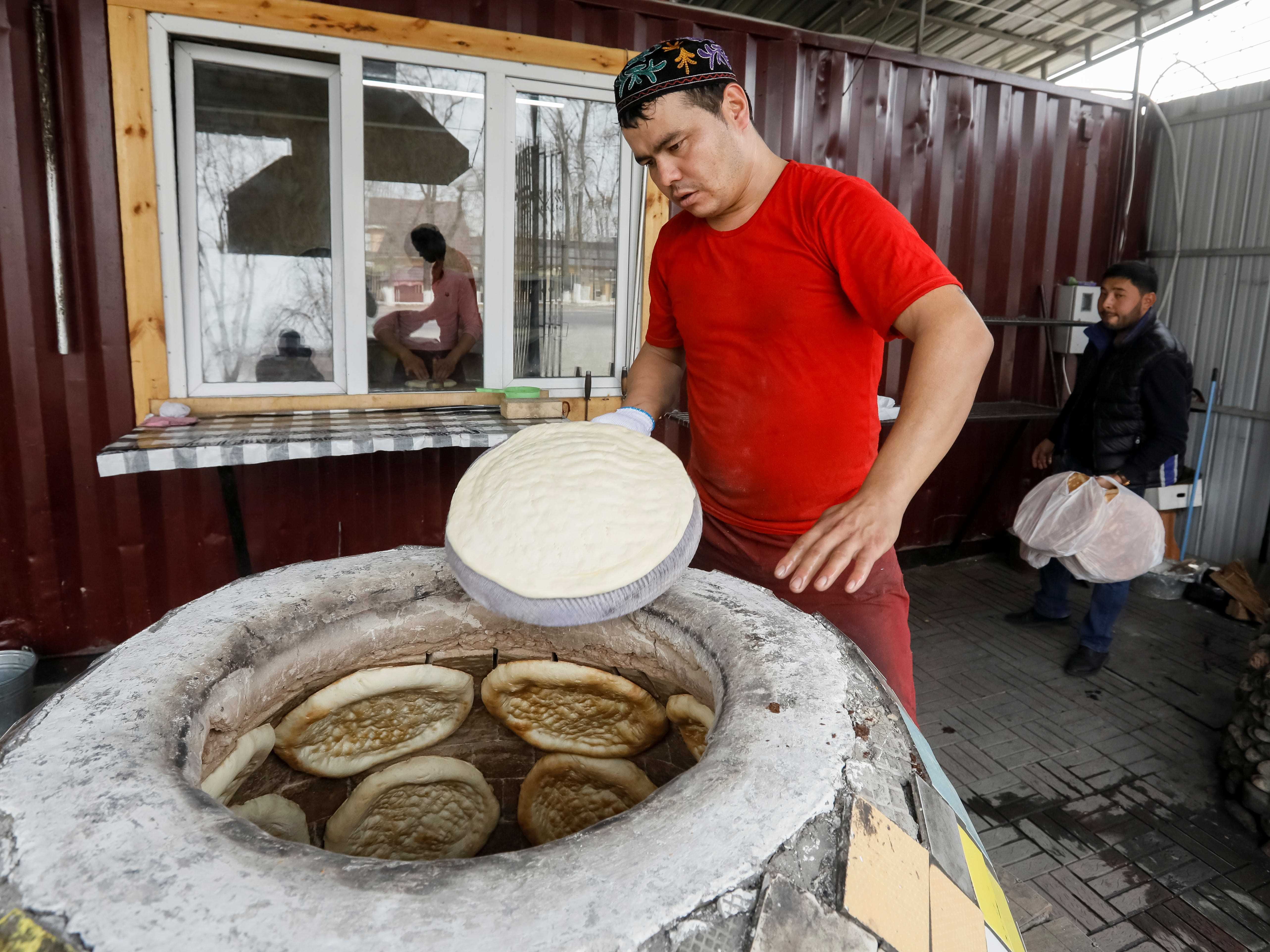 Ein Arbeiter legt einen Laib Brot in einen Tandyr-Lehmofen in einer Bäckerei in einem Dorf von Guldala, außerhalb von Almaty, Kasachstan.