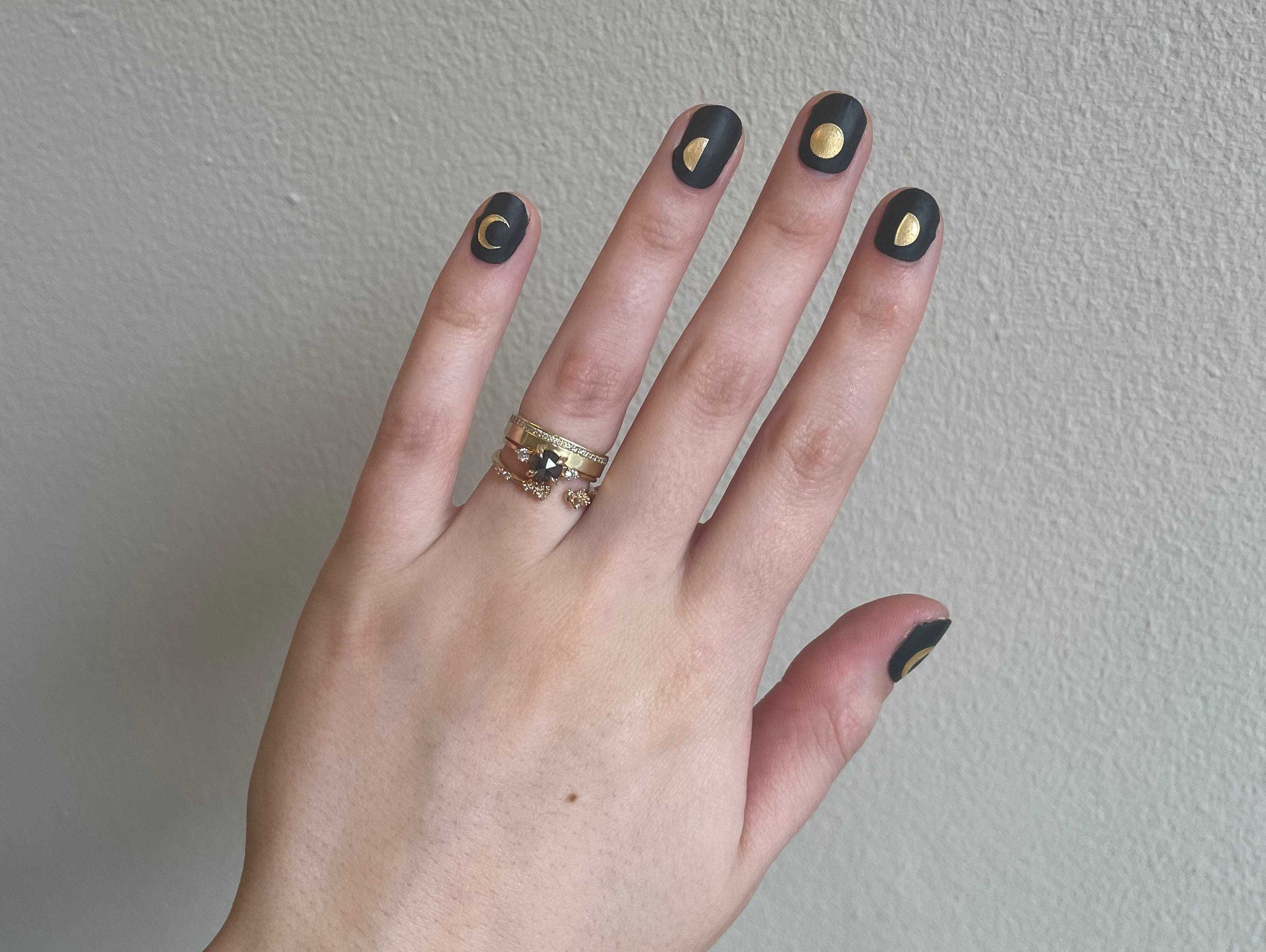 Schwarz-goldene Nagelsticker eines Handmodells von ManiMe, die Mondphasen darstellen.