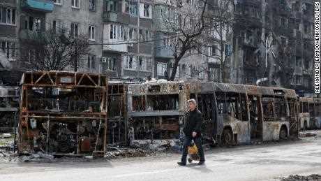 Ein Anwohner geht am 19. April 2022 in Mariupol eine Straße entlang, vorbei an ausgebrannten Bussen.