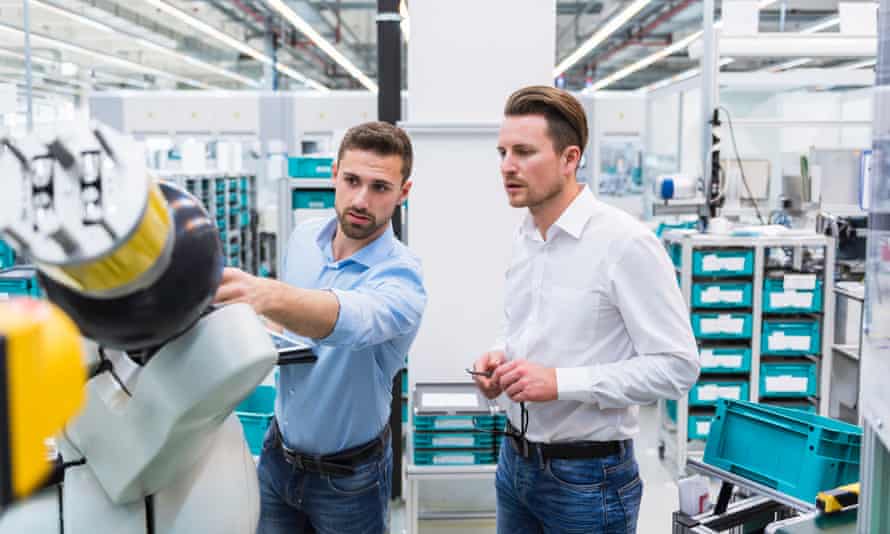 Zwei Männer mit Tablet untersuchen Montageroboter in der Fabrikhalle