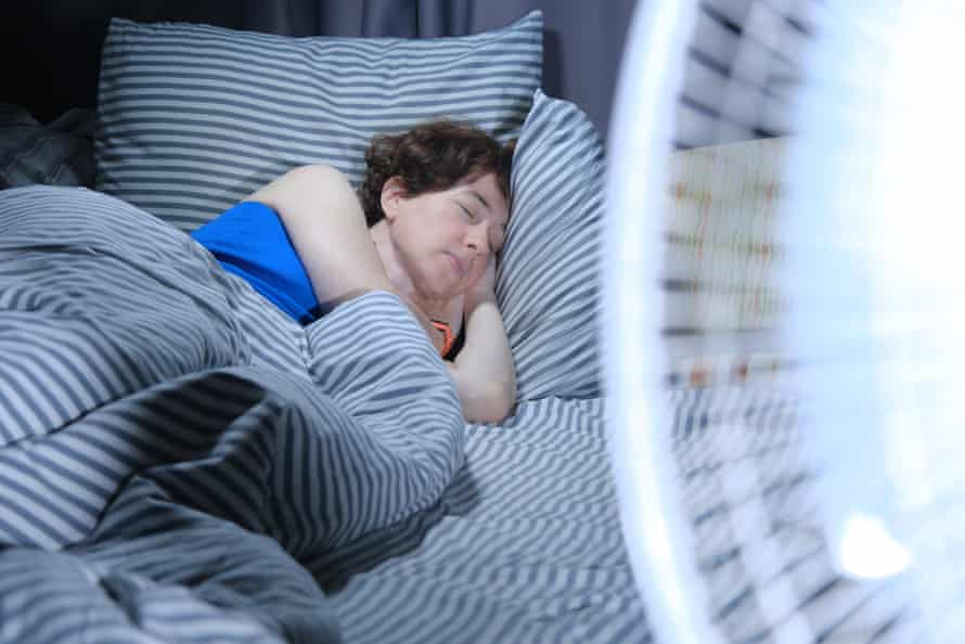 Frau schläft im Bett mit einem elektrischen Ventilator im Vordergrund